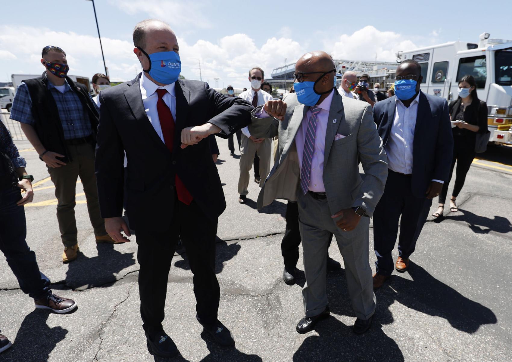 Denver Mayor Michael Hancock, right, and Colorado Governor Jared Polis greet each other by bumping elbows during an announcement that the City and County of Denver will launch a drive-up, COVID-19 test site in the parking lot of a downtown sports venue in an effort to stop the rise of the new coronavirus Thursday, May 21, 2020, in Denver. The free testing will be available daily for people who show symptoms of the coronavirus. City officials expect to administer more than 500 tests per day at the site, which opens Friday near the Pepsi Center. David Zalubowski