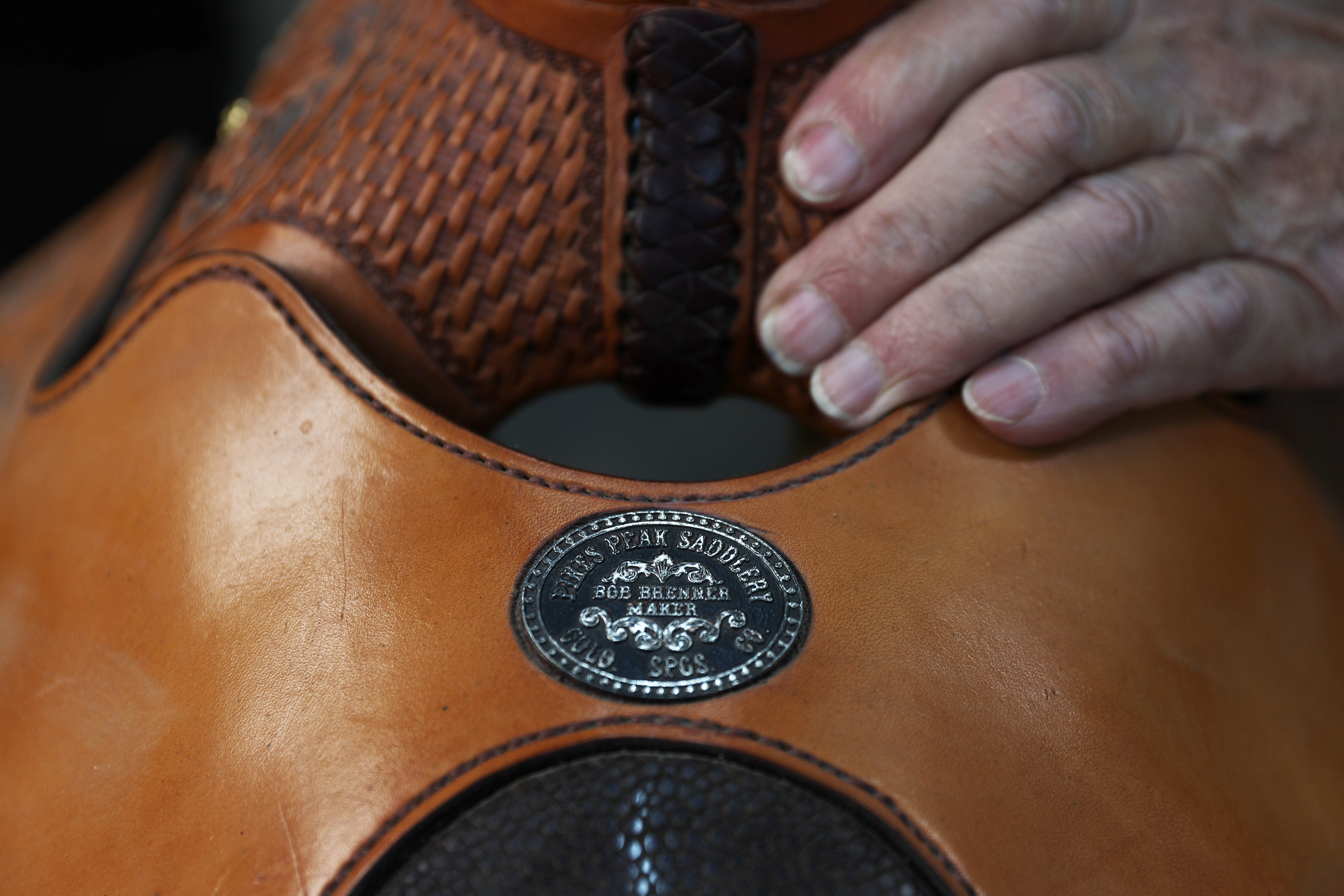 The emblem for Bob Brenner’s saddle shop sits on the seat rise of a saddle as he checks the position of the saddle skirt at his shop in Black Forest last month. (Forrest Czarnecki, The Denver Gazette)