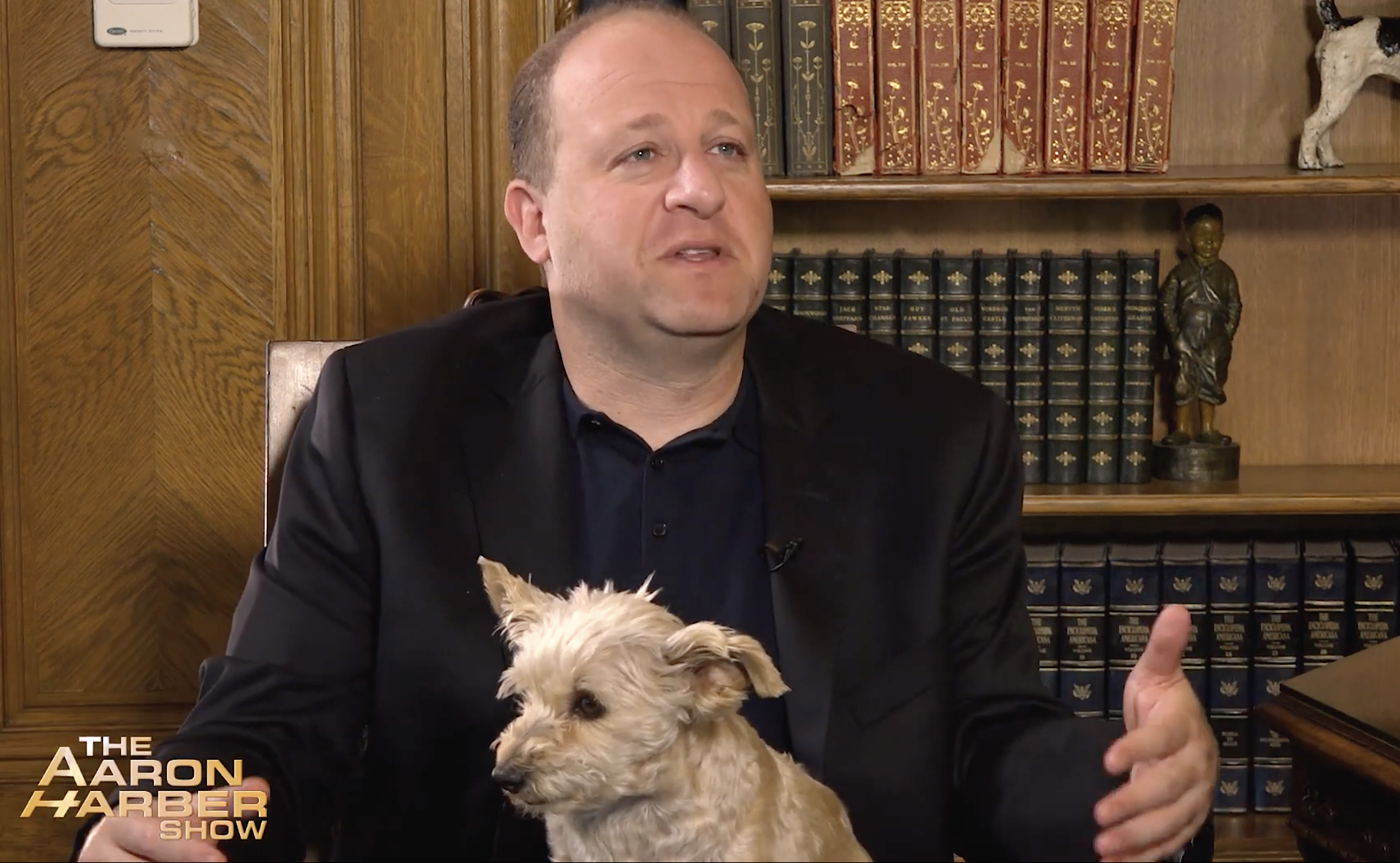 Gov. Jared Polis holds First Dog Gia during his chat with Aaron Harber for a program that will air statewide on Sunday. (Photo courtesy of “The Aaron Harber Show” via YouTube//)