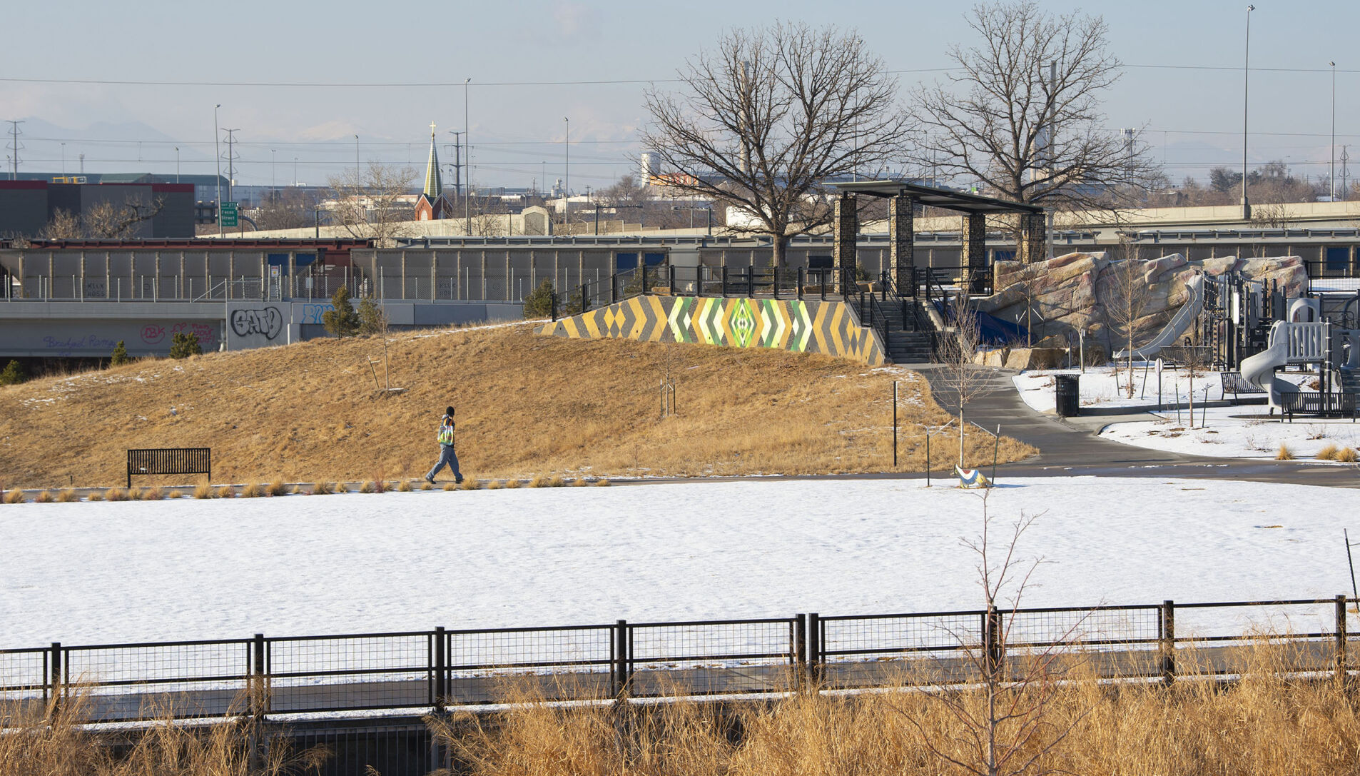 A pedestrian walks through Globeville Landing Park in December, with the Interstate 70 viaduct and the steeple of St. Joseph Polish Catholic Church in the background. (photos by Christian Murdock, The Gazette)