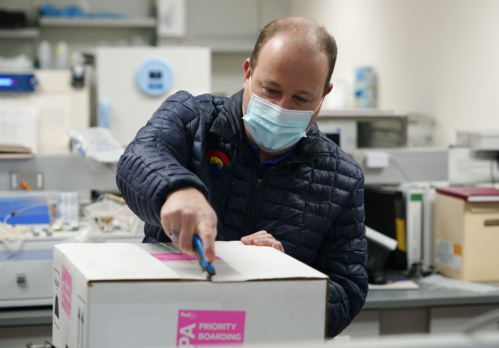 Gov. Jared Polis opens the state’s first shipment of COVID-19 vaccine at the Colorado Department of Public Health and Environment last week. (THE ASSOCIATED PRESS)