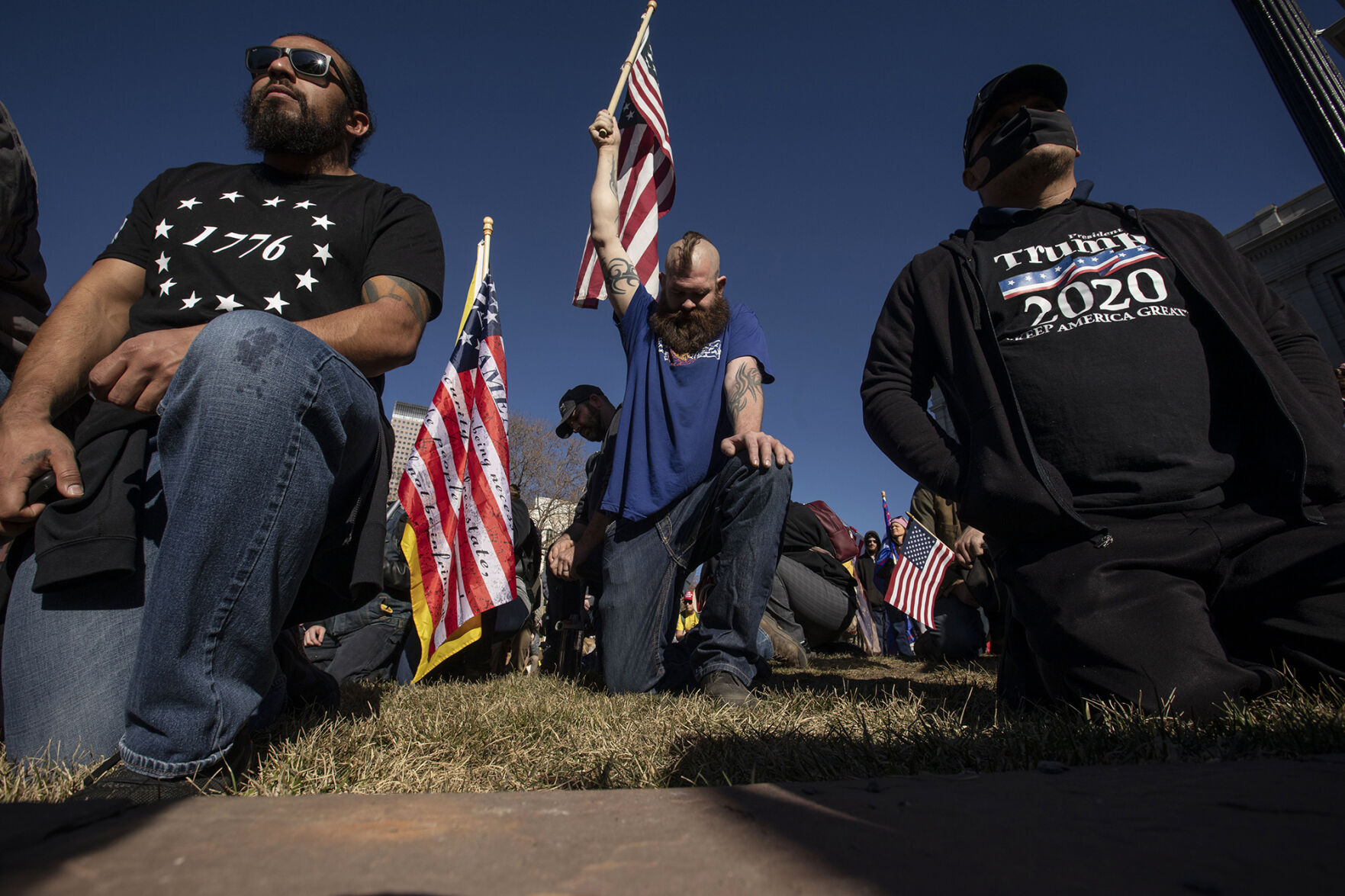 Jordan Schmidt, from Mead, kneels in prayer while holding an American flag during the 