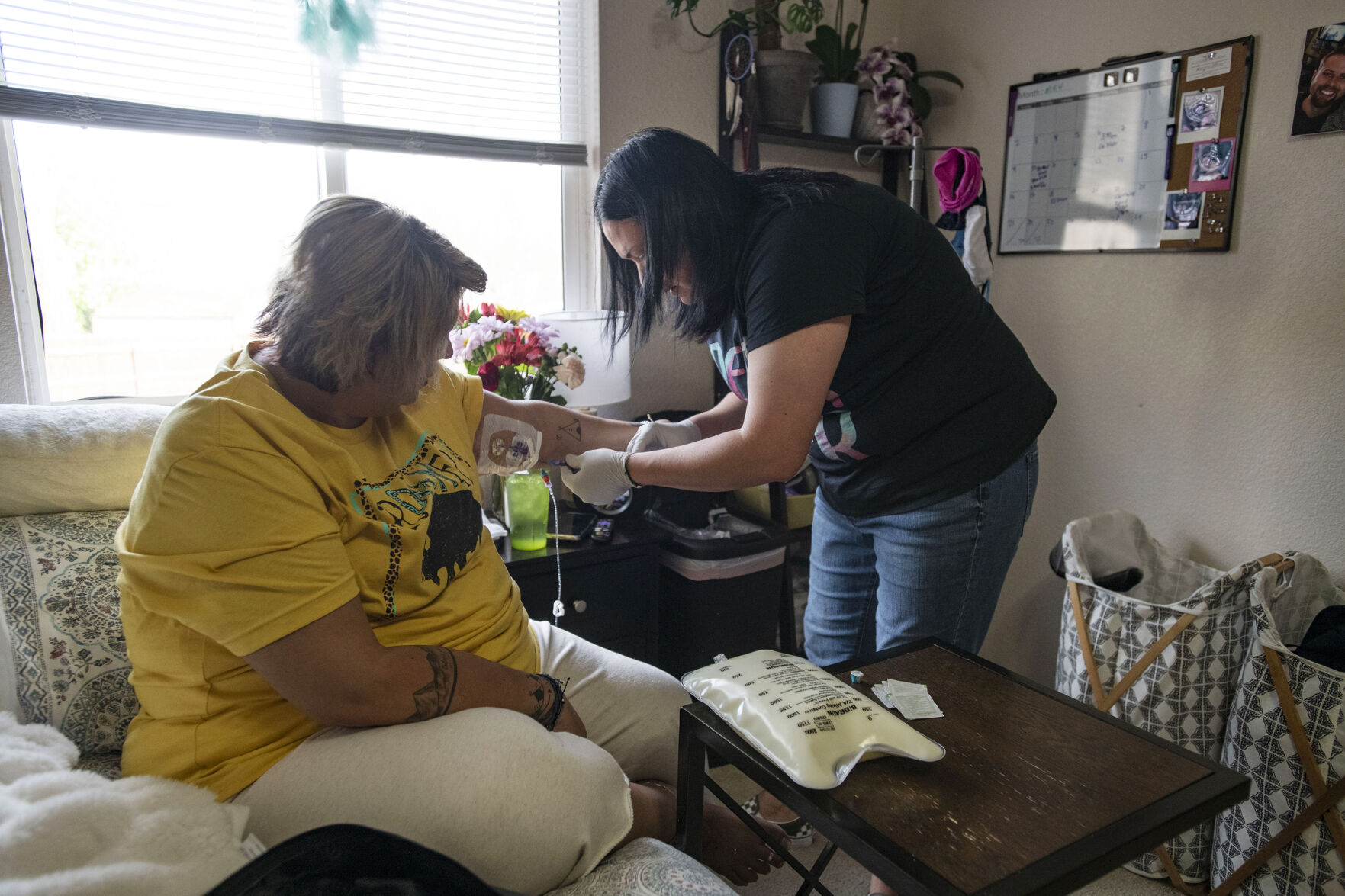 Brenna Logan, 37, helps her older sister Kendra Lippy, 38, change her TPN bag at Lippy's home in Colorado Springs on May 19, 2020. Logan helps her sister change her TPN bag every evening. The bag is needed for her to receive nutrients intravenously.  (Chancey Bush/ The Gazette) (Chancey Bush/ The Gazette)