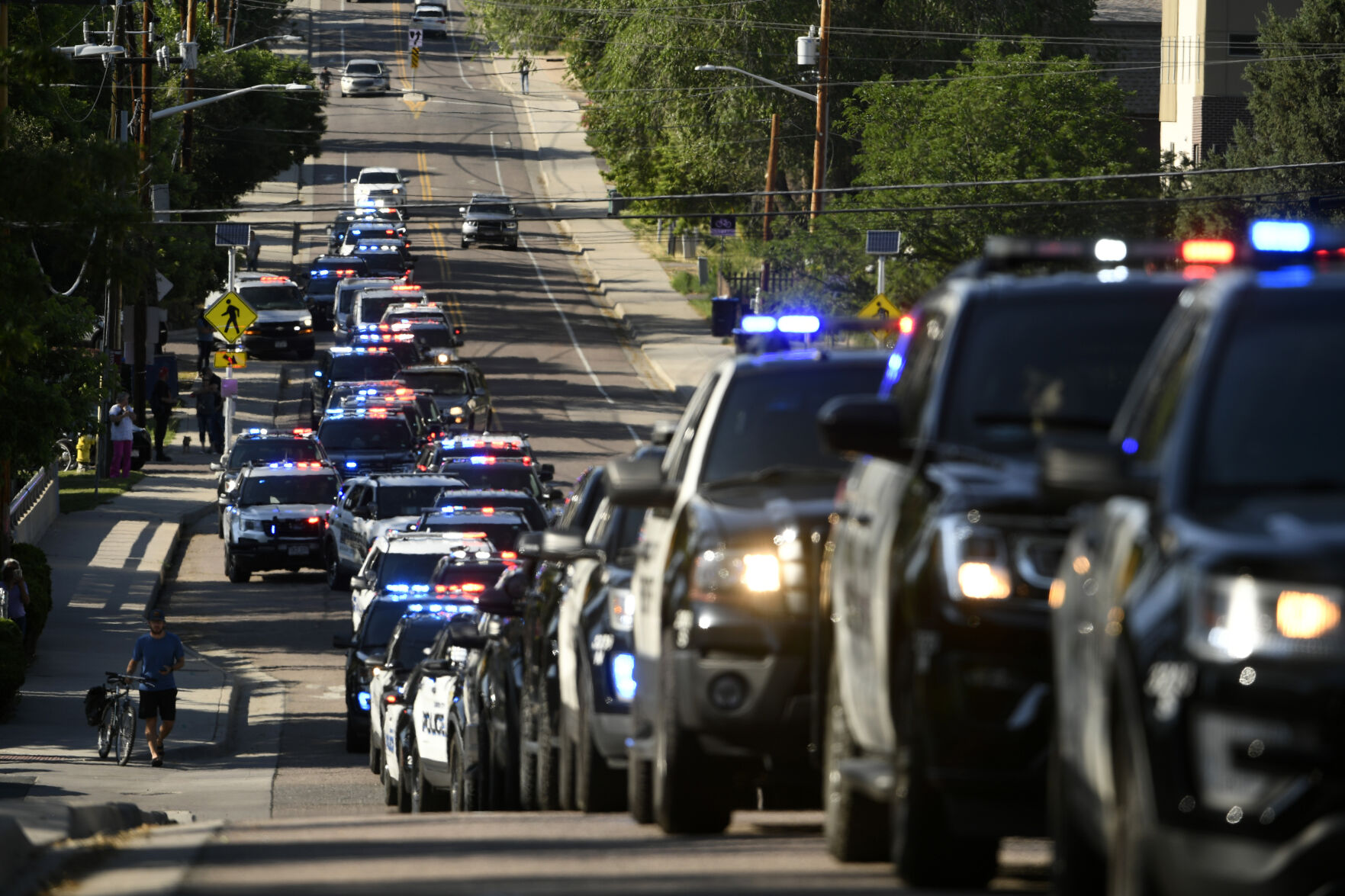 Dozens of police vehicles line up to take part in a procession held in the aftermath of a shooting in Olde Town Arvada that took the life of a police officer on Monday, June 21, 2021 in Arvada, Colo. Authorities say a gunman is believed to have shot and killed an officer and another person in a shopping district in a Denver suburb before being fatally shot by police. Police say an officer responded to a call about a suspicious incident Monday near the library in the city of Arvada, and about 15 minutes later, a 911 call came in about shots fired and the officer hit. (Helen H. Richardson/The Denver Post via AP) (Helen H. Richardson)