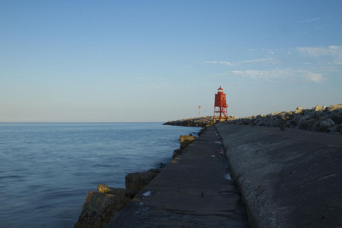 A red lighthouse at the end of a pier. Photo Credit: John_Brueske (iStock).