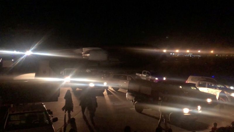 People walk past vehicles on the tarmac towards a plane at the airport in Kabul, Afghanistan, August 24, 2021, in this still image taken from video. REUTERS/via Reuters TV (REUTERS TV)