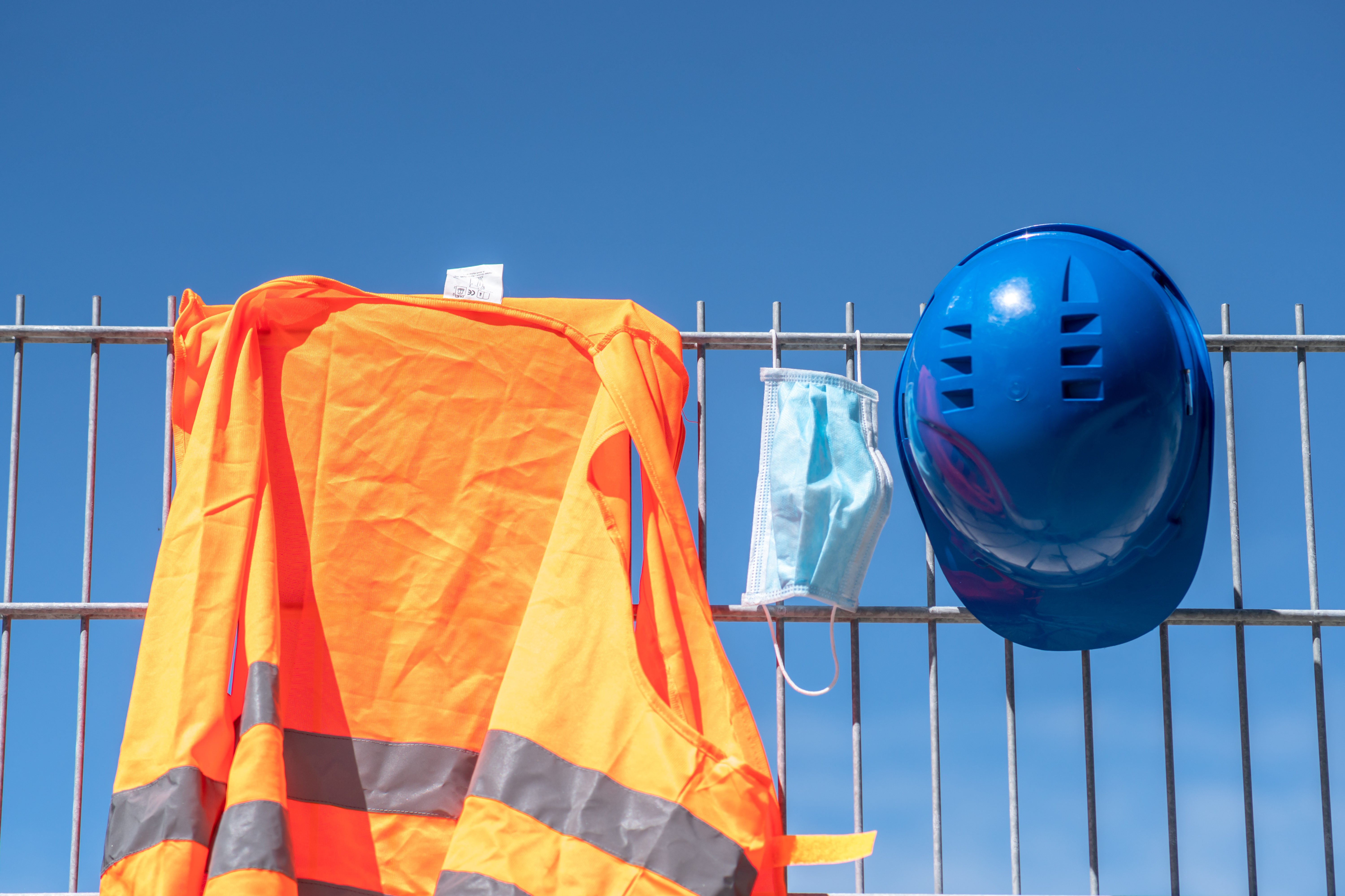 Occupational safety and protection against adverse conditions at work. Blue hard hat, reflective vest and protective surgical mask hanging on scaffolding (Cineberg)