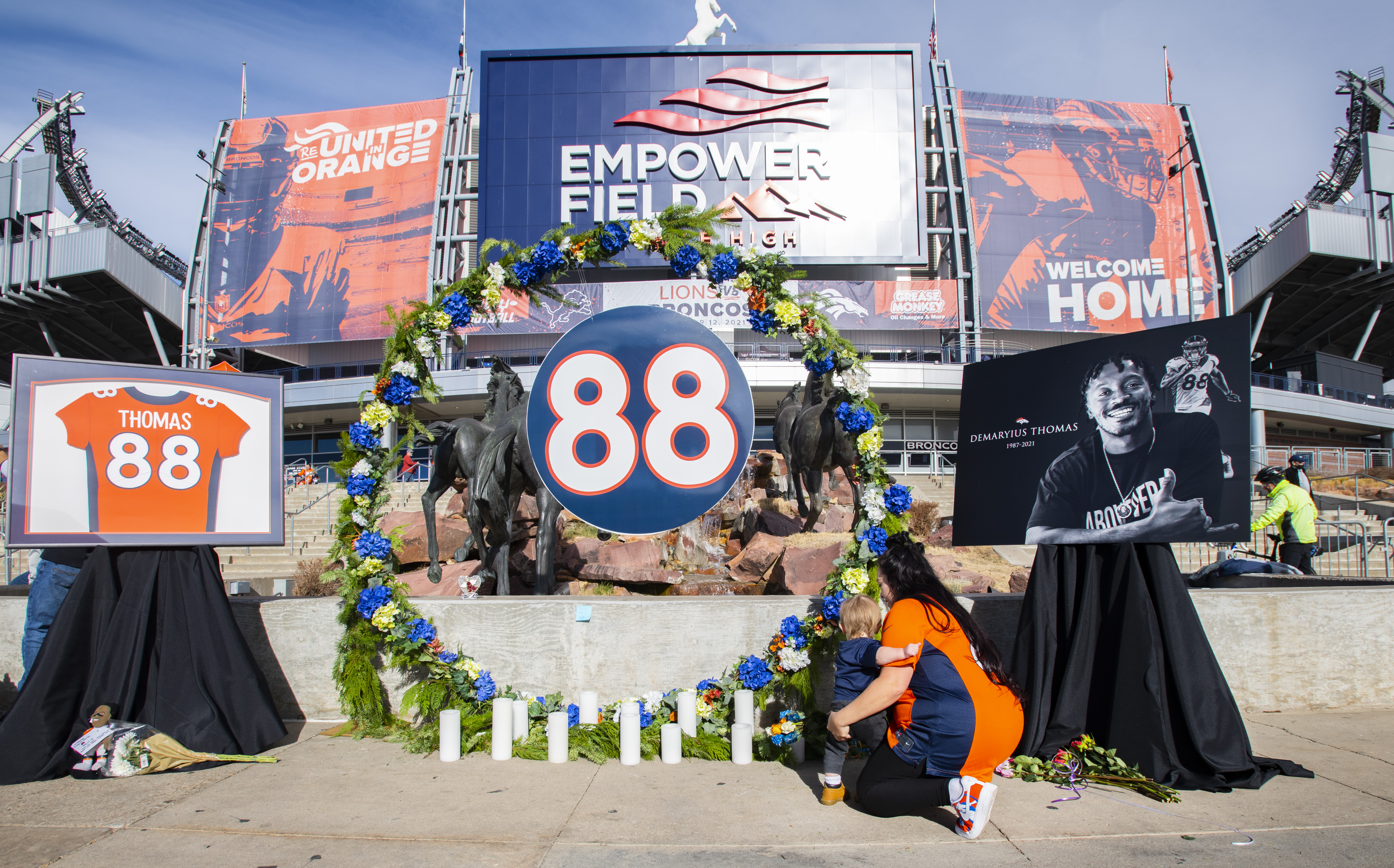 Selina Strock and her son, Ryker Childers, 1, place flowers at a memorial in the Ring of Fame Plaza Sunday, Dec. 12, 2021, for former Broncos wide receiver Demaryius Thomas before the start of the Broncos/Lions game at Empower Field at Mile High in Denver. Thomas died Thursday at the age of 33. He played 11 seasons in the NFL, nine with the Broncos. Strock and her family drove from Commerce City to pay tribute to their hero. They weren’t going to the the game. “He was my favorite player” Strock said. “Something about him made me love football. I’m hanging up my jersey and never wearing it again.” (The Gazette, Christian Murdock) (Christian Murdock/The Gazette)