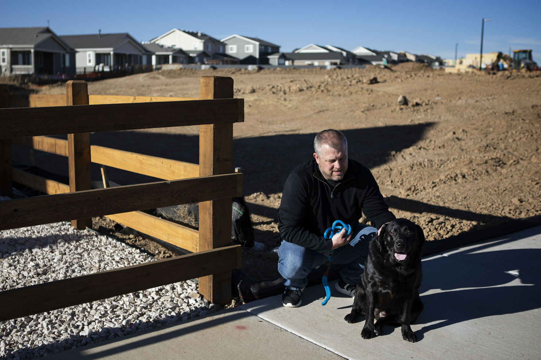 Resident Nick English pets his black lab Scarlet while construction on phase two of the Richmond American Homes development goes on in the background during a portrait session on Thursday, Dec. 2, 2021, in the Aurora Highlands Metro District in Aurora, Colo. (Timothy Hurst/The Gazette) (Timothy Hurst, The Gazette)