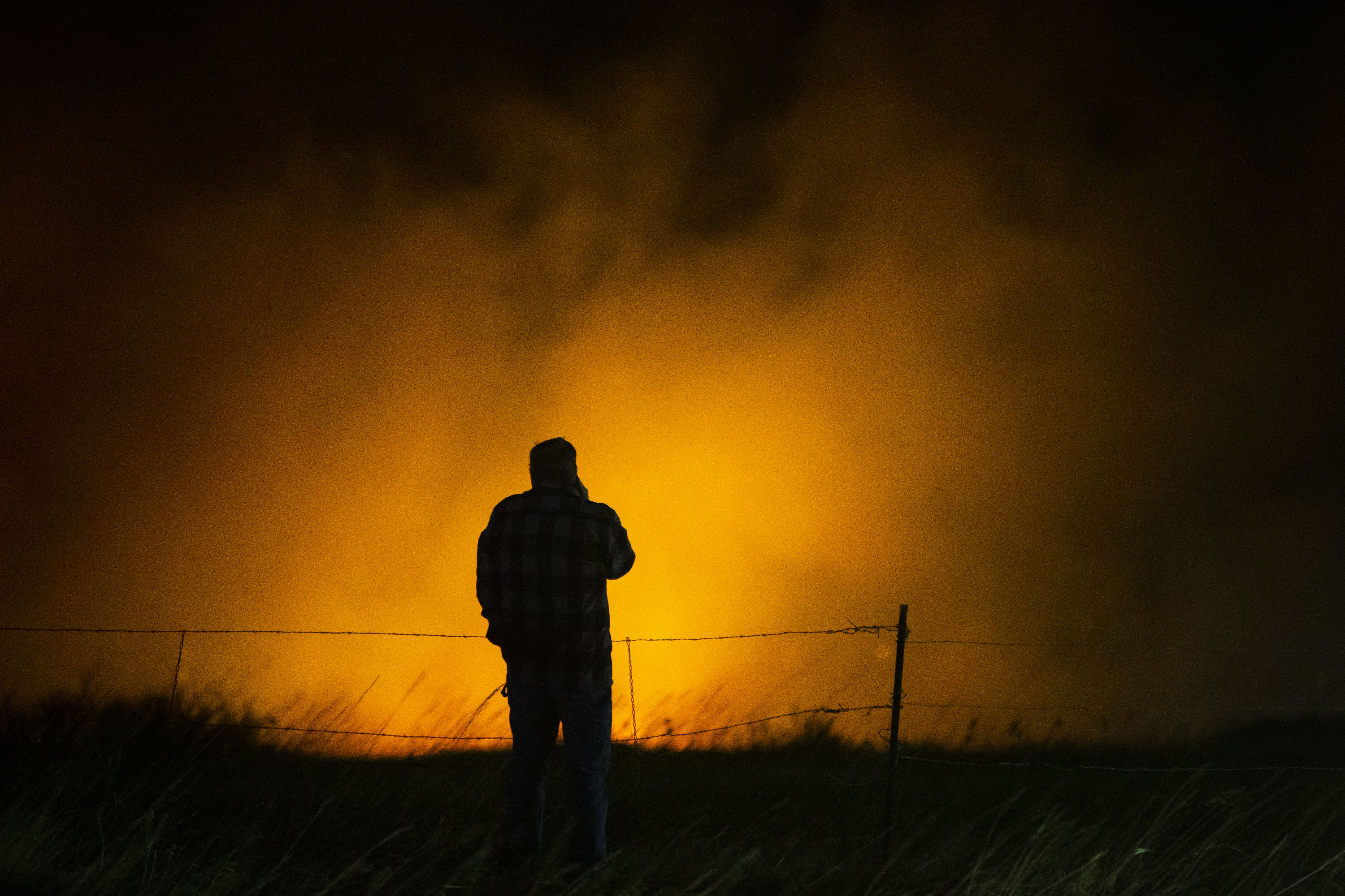 A person is backlit by glowing smoke as they overlook a fire moving through a neighborhood on Thursday, Dec. 30, 2021, in Superior, Colo. (Timothy Hurst/The Gazette) (Timothy Hurst)