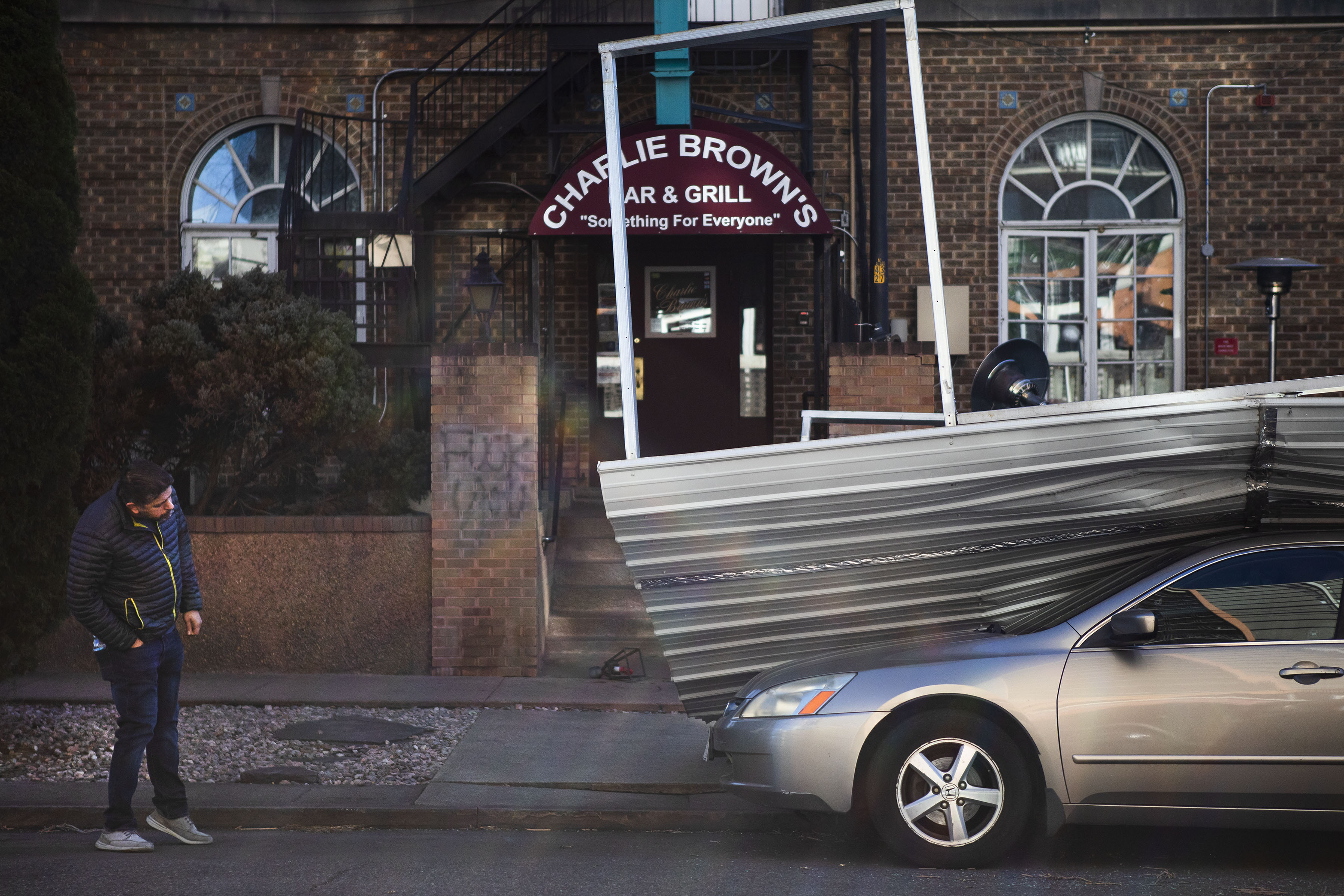 Charlie Brown’s Bar & Grill employee Stratis Katsaros looks at the damage of a metal roof that blew off the front porch and onto a parked car in front of the bar as Katsaros gets into work on Wednesday, Dec. 15, 2021, in Denver, Colo. (Timothy Hurst/The Gazette) (Timothy Hurst)