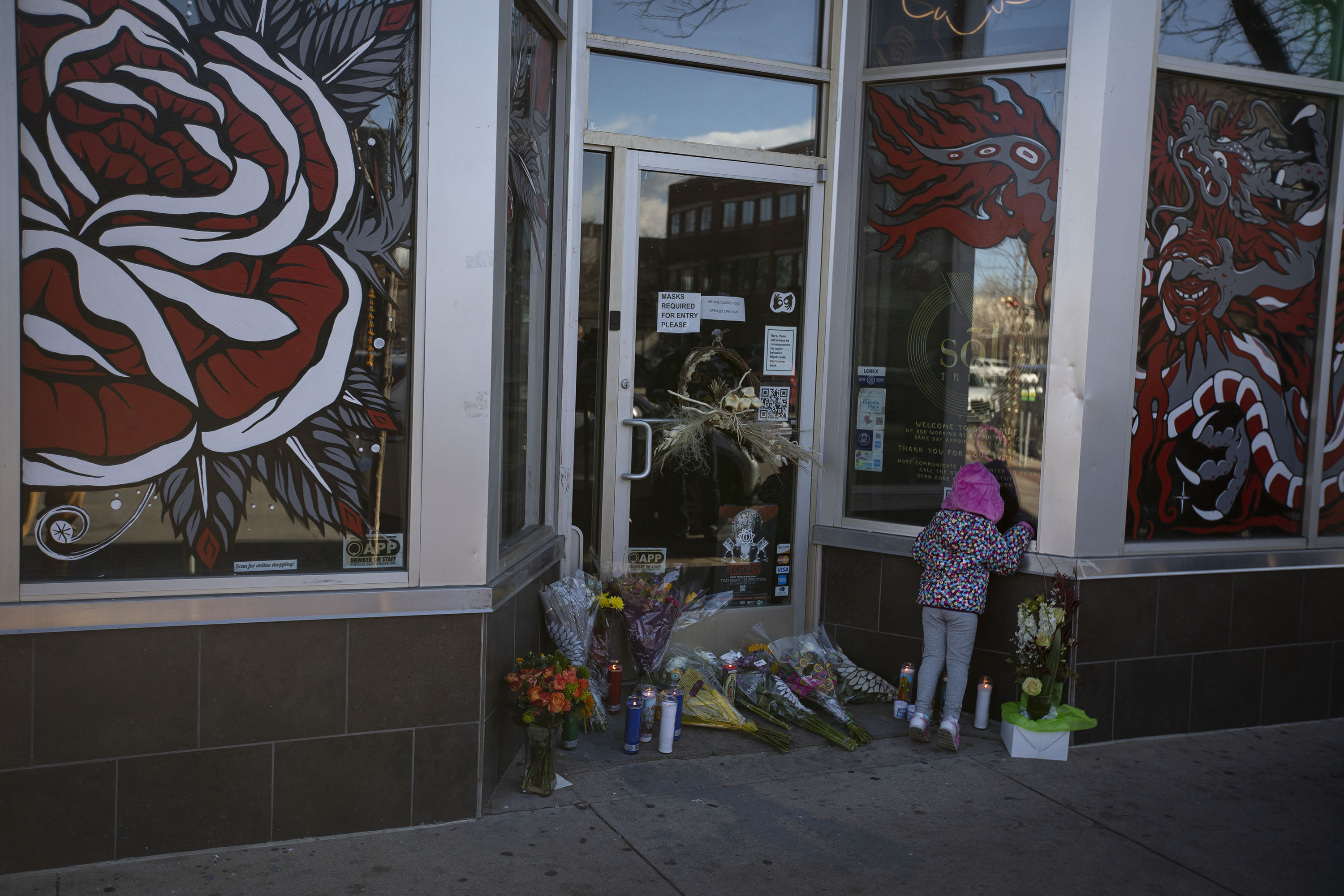A child peers into the front window of Sol Tribe Tattoo & Piercing while standing next to flowers and candles dropped off for slain shop owner Alicia Cardenas on Tuesday, Dec. 28, 2021, in Denver, Colo. (Timothy Hurst/The Gazette) (Timothy Hurst)