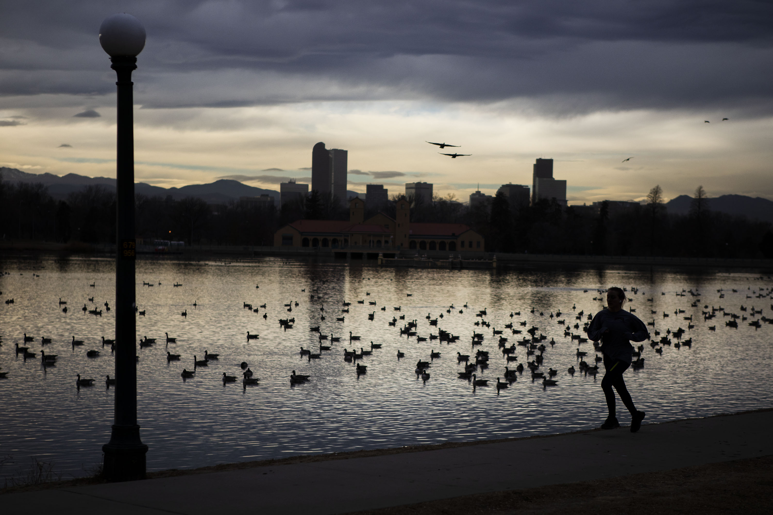 Light spills in from behind the Denver skyline as a runner makes their way past Ferril Lake in City Park on Wednesday, Dec. 8, 2021, in Denver, Colo. (Timothy Hurst/The Gazette) (Timothy Hurst)