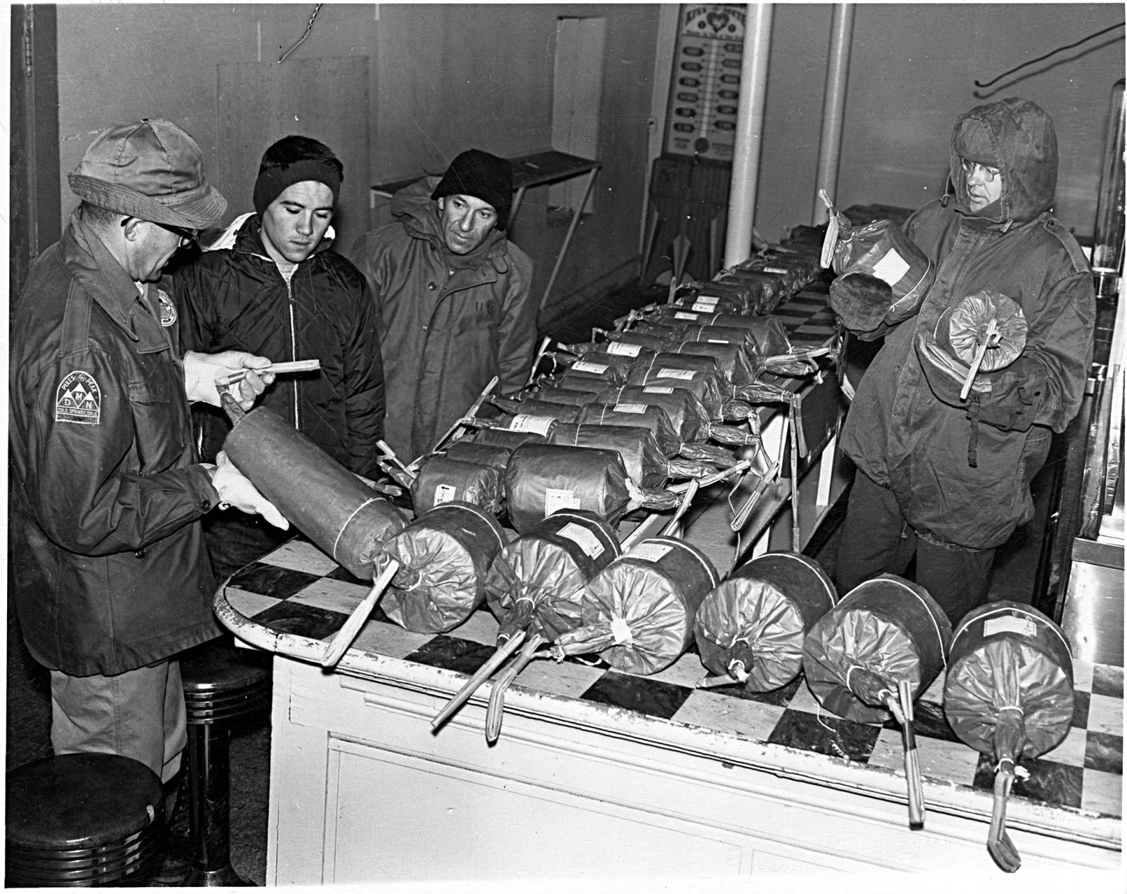 Four men study a line of wrapped fireworks on a checkered countertop for the Pikes Peak AdAmAn Club in 1965. The photograph is identified on the back as: “In summit house — fire works being prepared for display — 1965? 1. Bob Ellingwood. 2. — 3. — Dr. Alson Pierce 4. — Dr. Geo. Lindaman at Pikes Peak Summit House.” The photographer is unknown. The annual celebration started in 1922 when five mountaineers — including Fred Barr — loaded their packs with about 200 pounds of rockets, flares and fireworks and set out to mark the new year with the first recorded winter ascent of America’s Mountain. (Margaretta M. Boas Photograph Collection, Courtesy of Pikes Peak Library District, 001-4616)