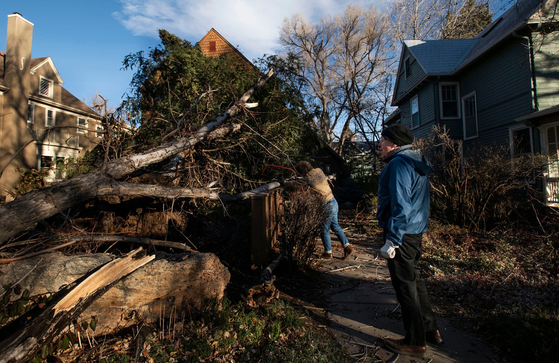 Robert Lee, retired Colorado College professor, right, takes a moment of pause as Benedict Wright helps saw branches after a large evergreen tree and half of an ash tree blew over at Lee’s home on Tejon Street near Buena Ventura Street in the Old North End neighborhood of Colorado Springs on Wednesday, Dec. 15, 2021. Wright, CC alumni Class of 2020, was visiting Lee for the day. Lee has lived at his home since 1982. “I’m grateful that the damage doesn’t seem to be greater than it is and no one got hurt,” said Lee. (Chancey Bush/ The Gazette) (Chancey Bush/ The Gazette)