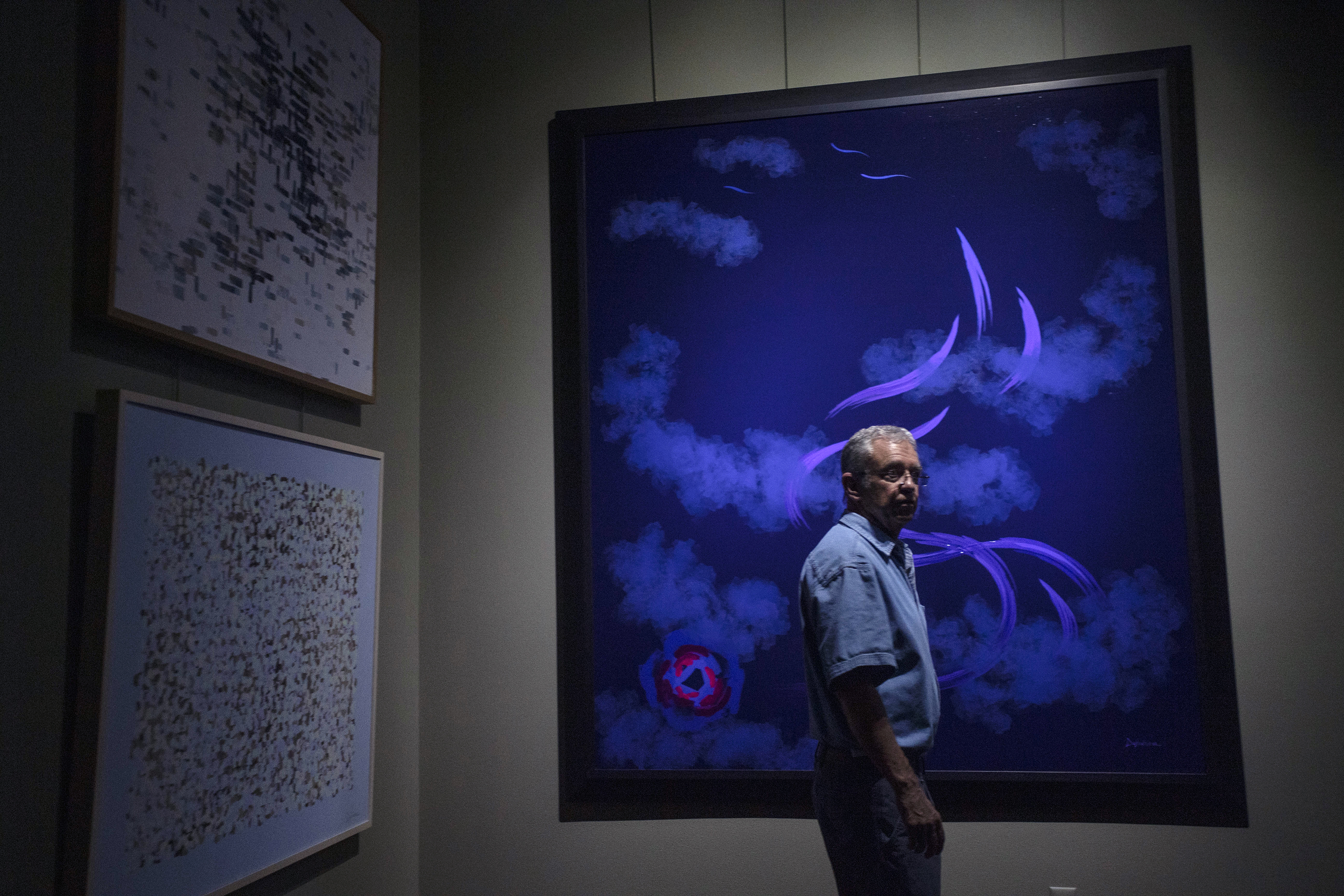 Paul Kirby, at his studio in Loveland, stands in front of “Meditation Upon Death.” The painting was produced by Dulcinea, a robot artist he invented that paints one-of-a-kind art based on computer simulations coded by Kirby. He was trying to capture his love for his wife, Linda, and his sadness that she was gone. (Chancey Bush, The Gazette)