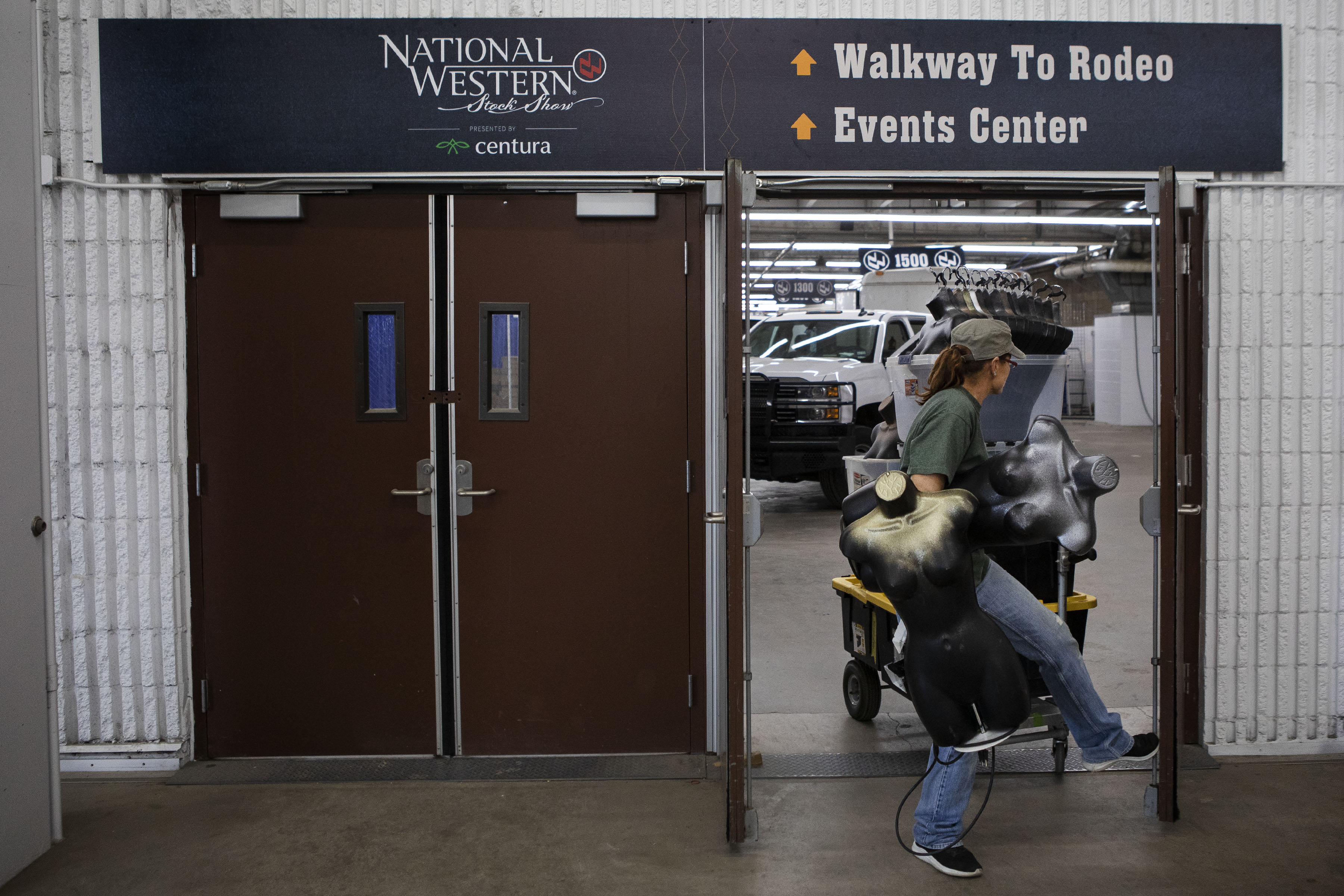 Renee Kallio opens a door with her foot as she carries mannequins and pulls a box of merchandise to a trailer for her friend and owner of Cowgirl Glitter western wear, based in Galveston, Texas, at the National Western Stock Show’s Hall of Education on Monday, Jan. 24, 2022, in Denver, Colo. (Timothy Hurst/The Gazette) (Timothy Hurst)