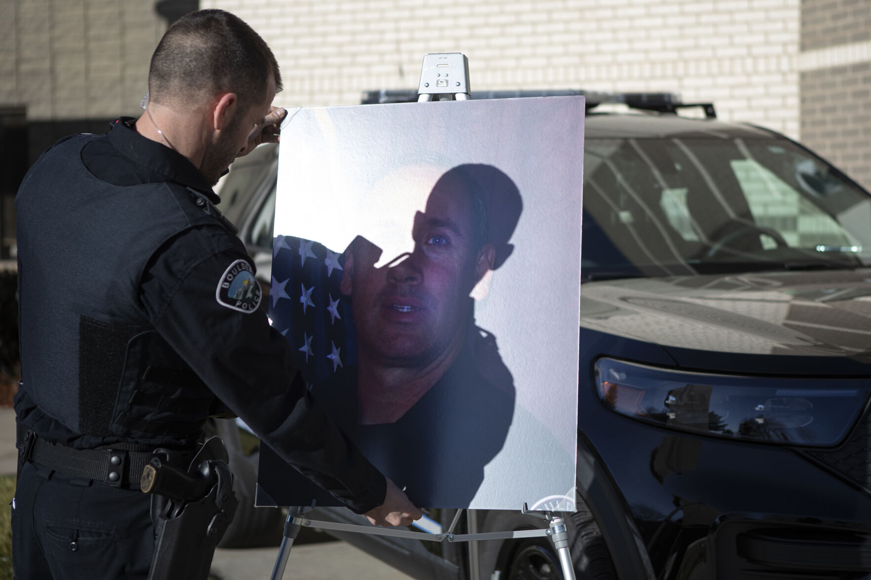 Boulder Police officer David Middlebrooks straightens a photo of slain officer Eric Talley, who was killed while responding to the mass shooting at the King Soopers grocery store on Table Mesa Drive nearly one year ago, at a memorial site including a police cruiser set up in front of the police department on Friday, March 18, 2022, in Boulder, Colo. (Timothy Hurst/The Denver Gazette) (Timothy Hurst)