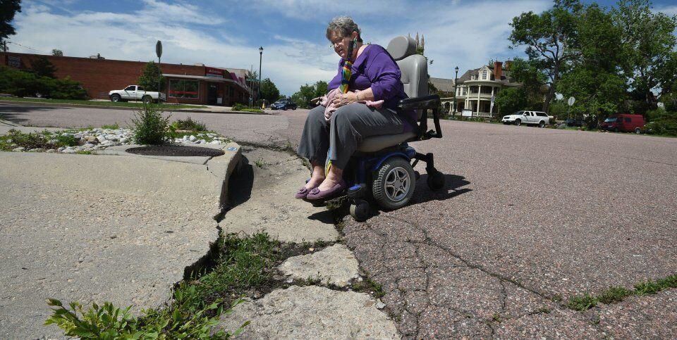 Sharon King, who uses a power wheelchair, said she has problems commuting around downtown Colorado Springs because of cracked roads, bad street lighting and no connecting curb cuts between sidewalks. King shows a curb in 2015 at Willamette Avenue and Tejon Street that has a curb cut that has become so damaged that she got stuck there in her chair. ((Photo by Jerilee Bennett, The Gazette))