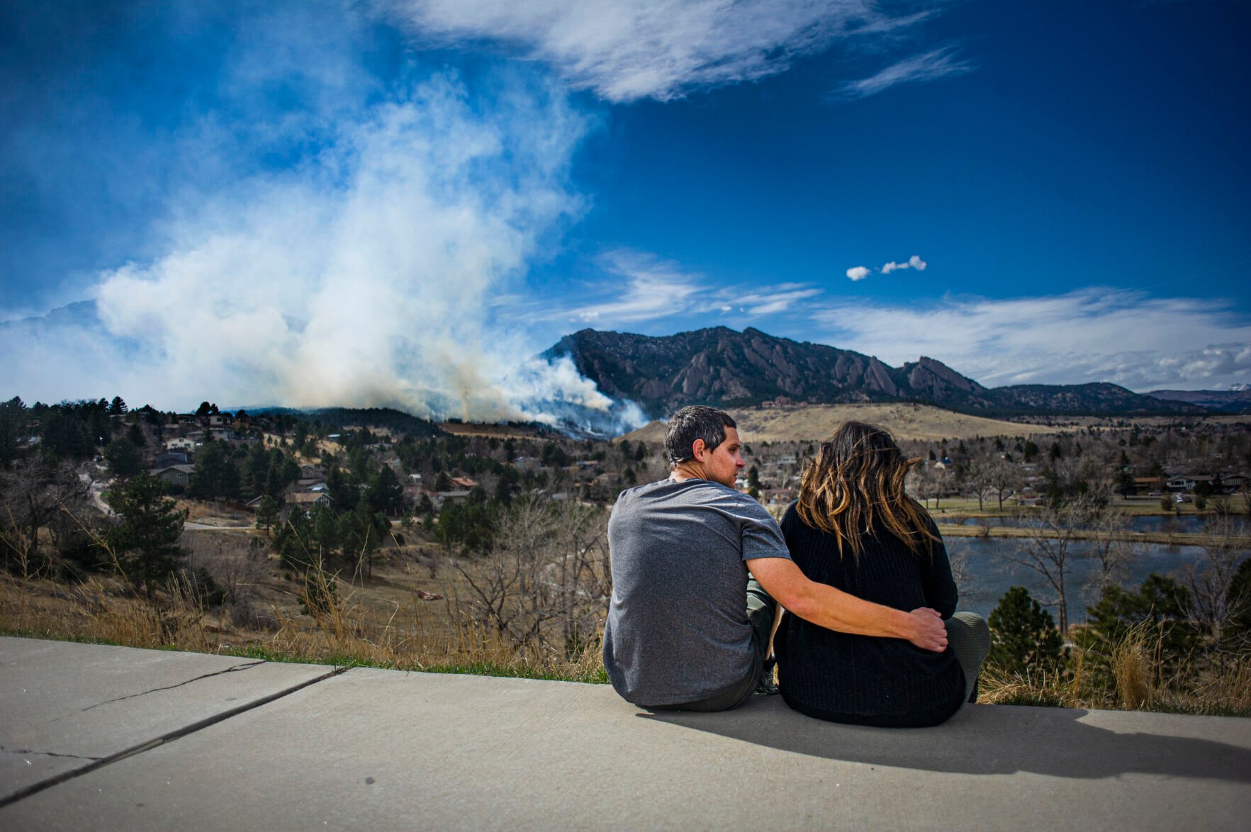 Nick Grossman comforts his partner Chelsea Castellano, as they watch smoke from the NCAR Fire from the safety of Fairview High School on March 26, 2022, in Boulder, Colo. They own a home in the evacuated Shanahan Ridge neighborhood. (Jacob Byk/ For The Denver Gazette)