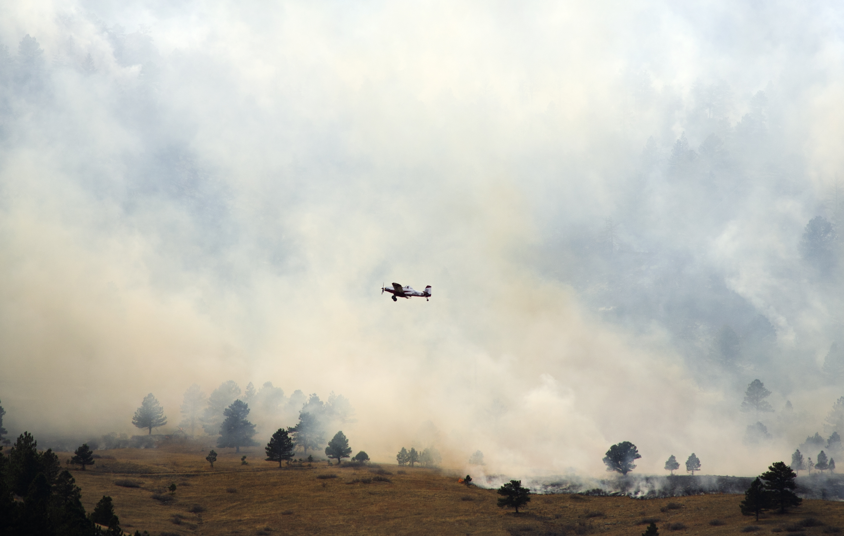 A plane flies low over flames and smoke from the NCAR Fire on March 26, 2022, in Boulder, Colo. (Jacob Byk/For The Denver Gazette)