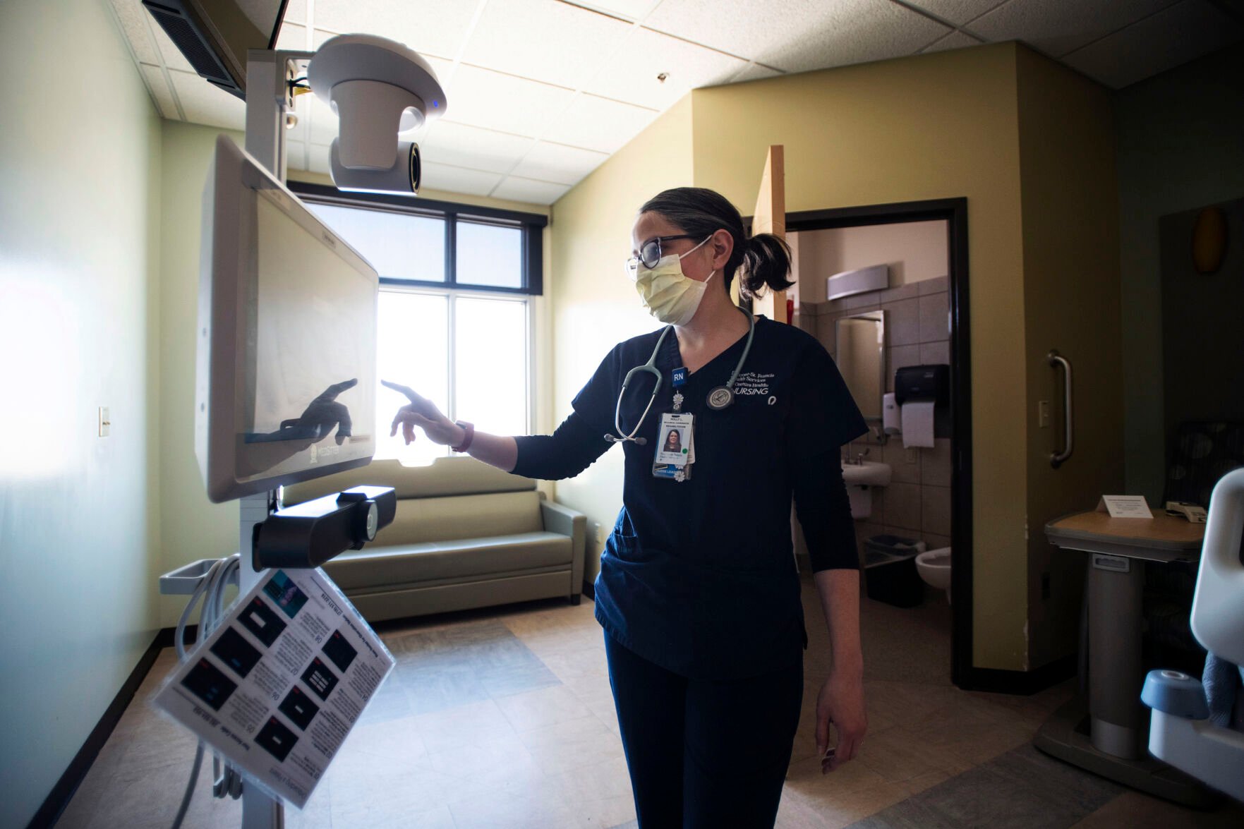 Holly Lawson, clinical coordinator at St. Francis Hospital, demonstrates how the new camera monitor system works inside a room at St. Francis Hospital in Colorado Springs on Friday, March 25, 2022. Penrose- St. Francis is expanding the use of cameras that can monitor patients who might otherwise need a staff member in the room constantly. Hospitals, nursing homes and the broader health system face a long road to recovery from the staffing shortages. (Chancey Bush/ The Gazette) (Chancey Bush/ The Gazette)