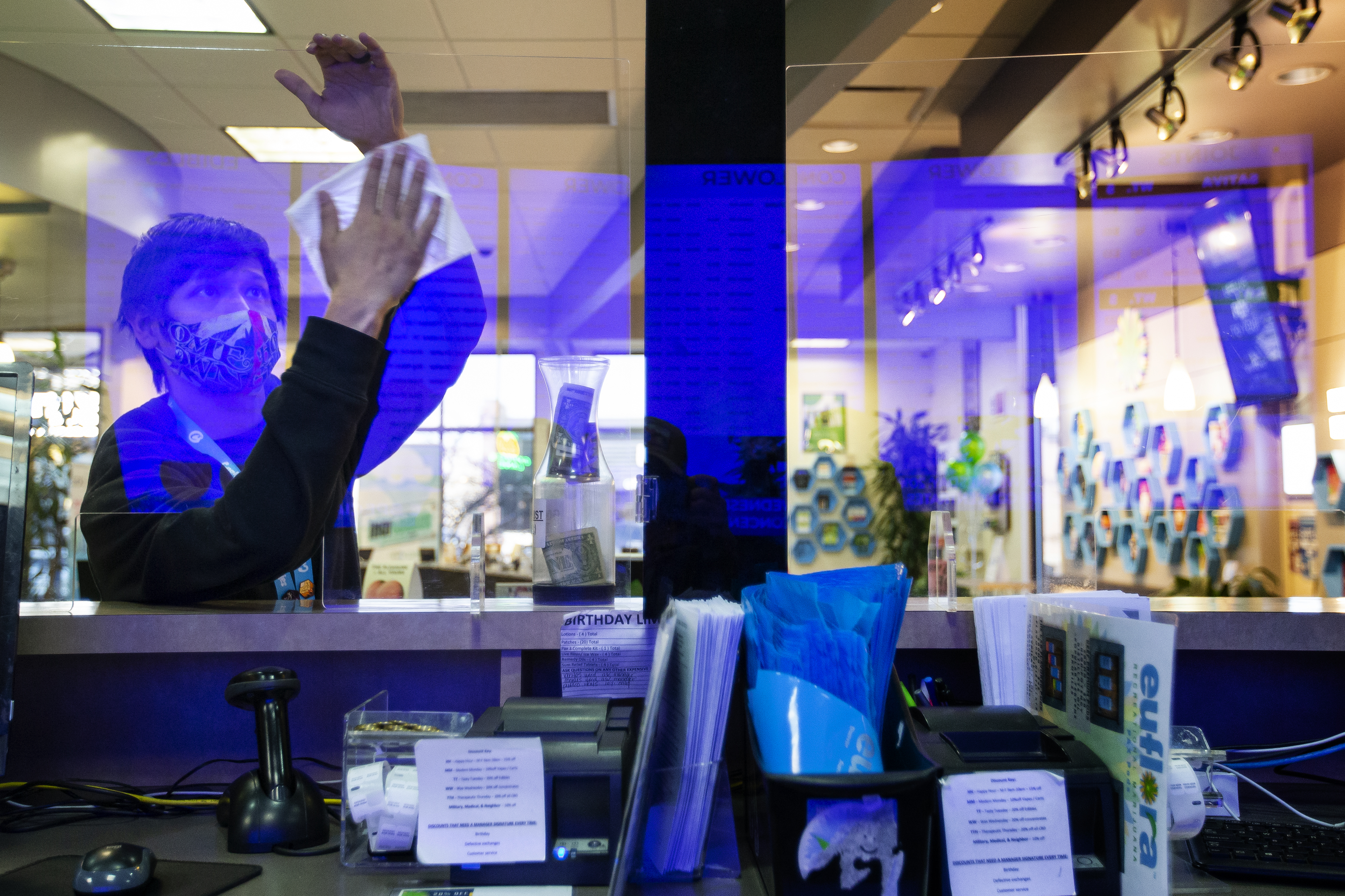 Budtender Daniel Guerrero takes a moment to clean the plexiglass dividers at the front counter at the Euflora Recreational Marijuana Dispensary on Wednesday, Feb. 23, 2022, in Aurora, Colo. (Timothy Hurst/The Denver Gazette)