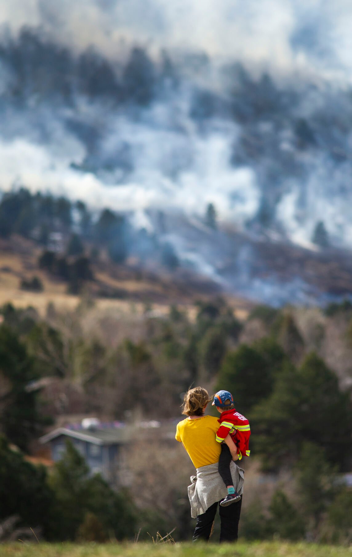 Christina Madsen holds her three-year-old son, Marius, while watching the smoke of the NCAR Fire from the safety of Fairview High School on March 26, 2022, in Boulder, Colo. They evacuated their home in the Shanahan Ridge neighborhood. (Jacob Byk/For The Denver Gazette)