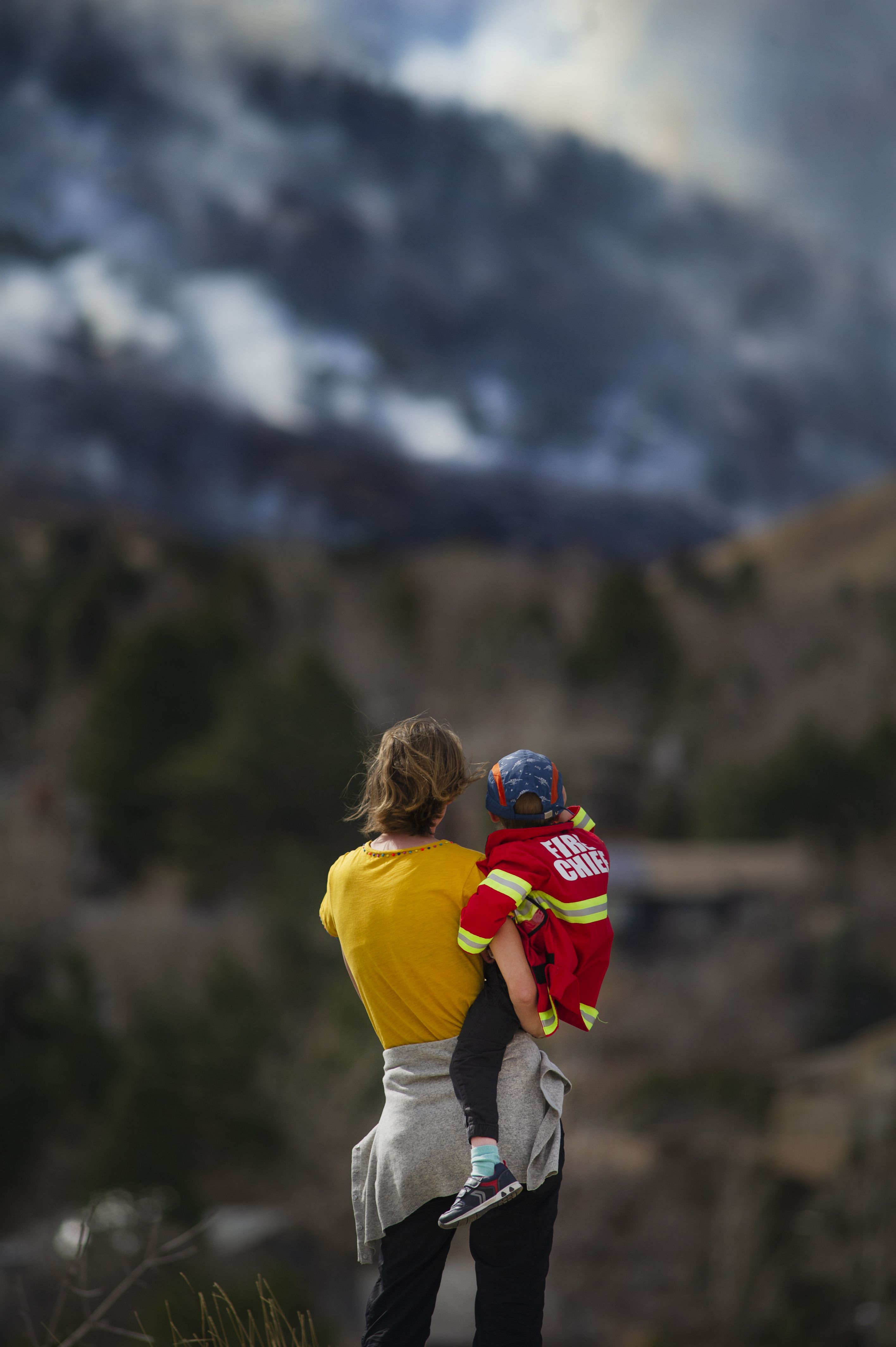 Christina Madsen holds her three-year-old son, Marius, while watching the smoke of the NCAR Fire from the safety of Fairview High School on March 26, 2022, in Boulder, Colo. They evacuated their home in the Shanahan Ridge neighborhood. (Jacob Byk/For The Denver Gazette)