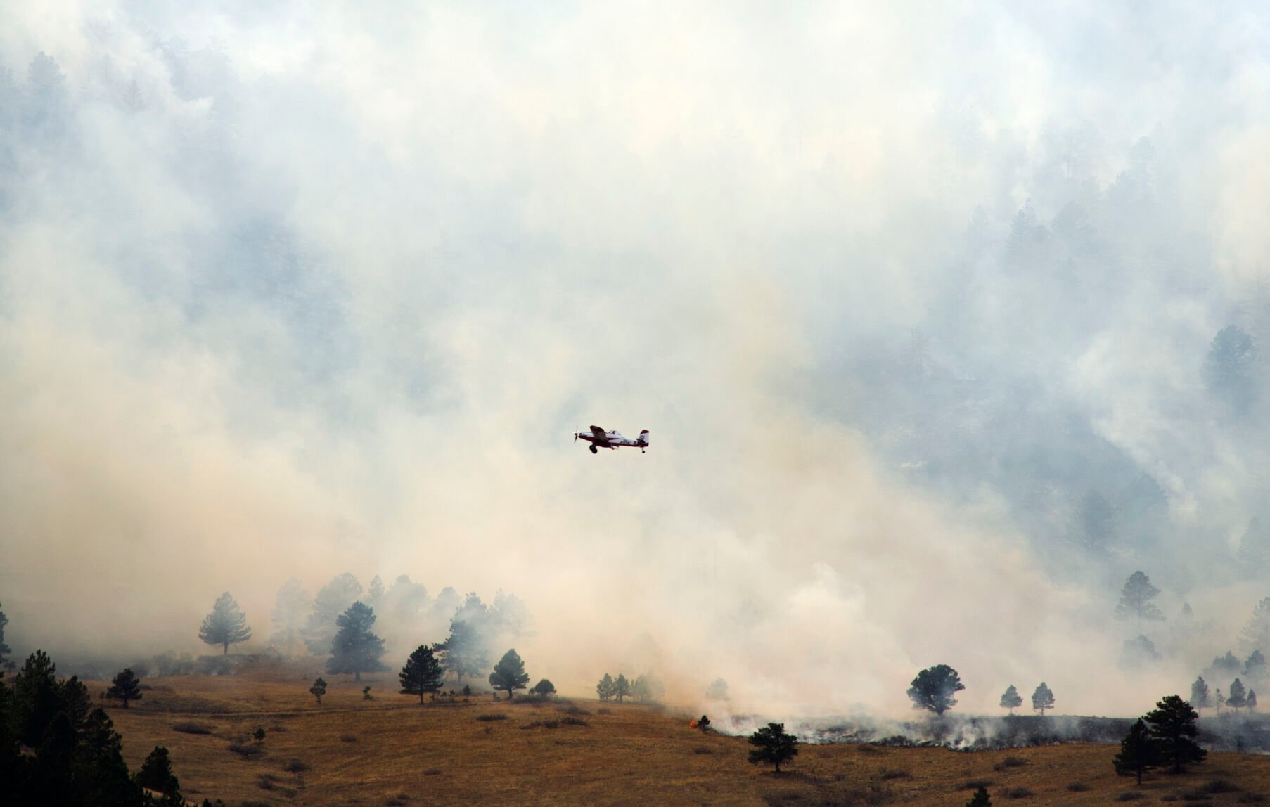 A plane flies low over flames and smoke from the NCAR Fire on March 26, 2022, in Boulder, Colo. (Jacob Byk/For The Denver Gazette)