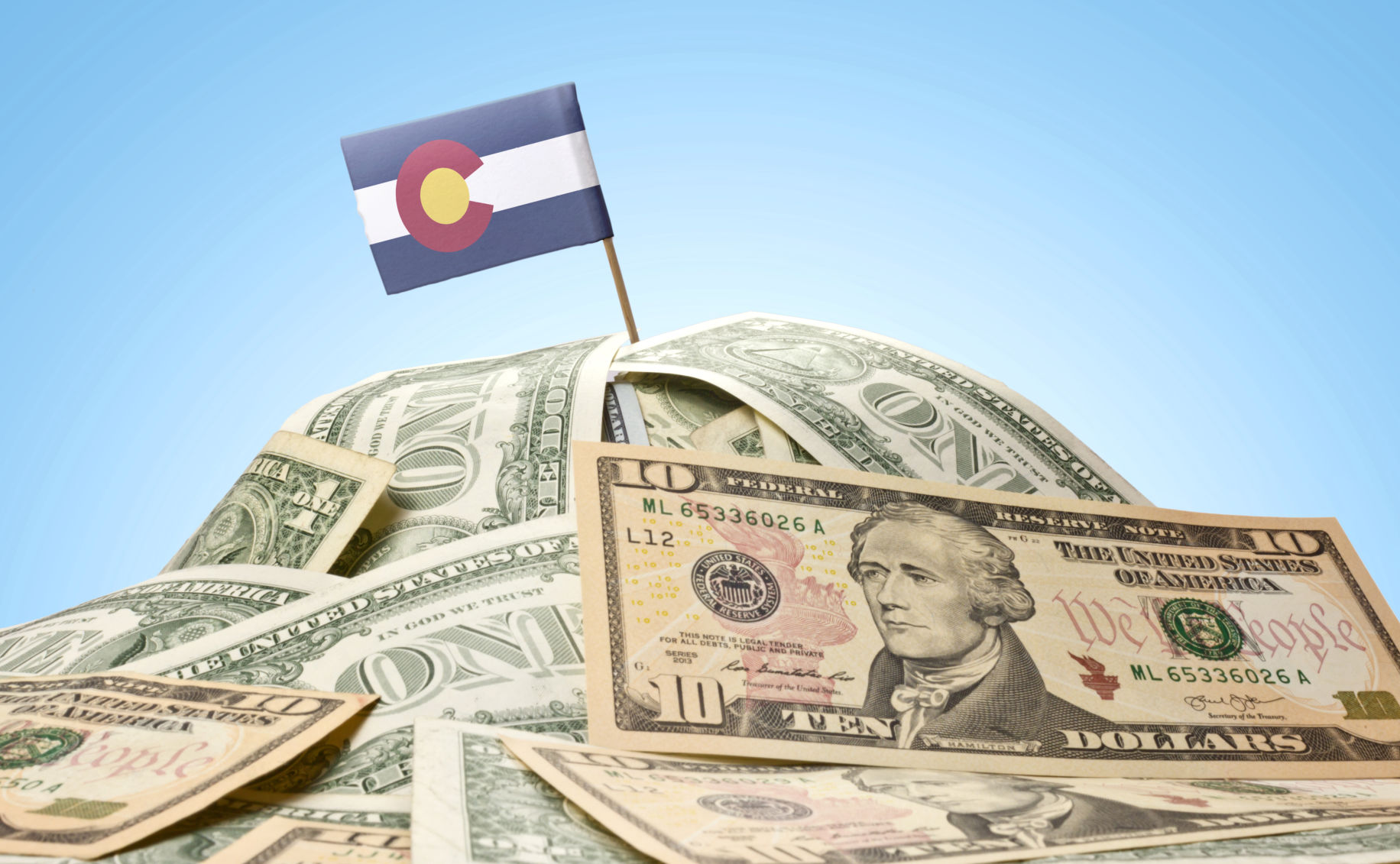 The state flag of Colorado sticking in a pile of U.S. dollars. (eyegelb, istock)