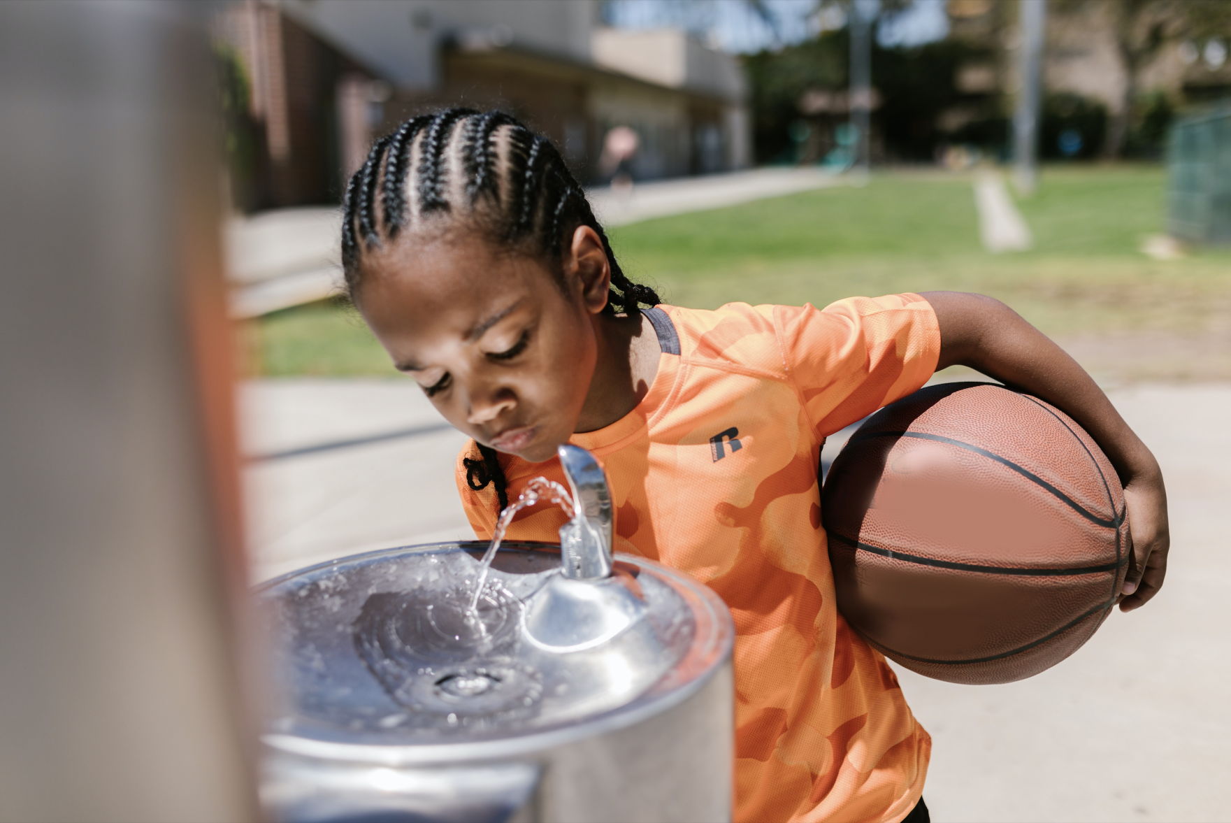 A boy drinks from a water fountain in a basketball school park (RODNAE Productions/Pexels)