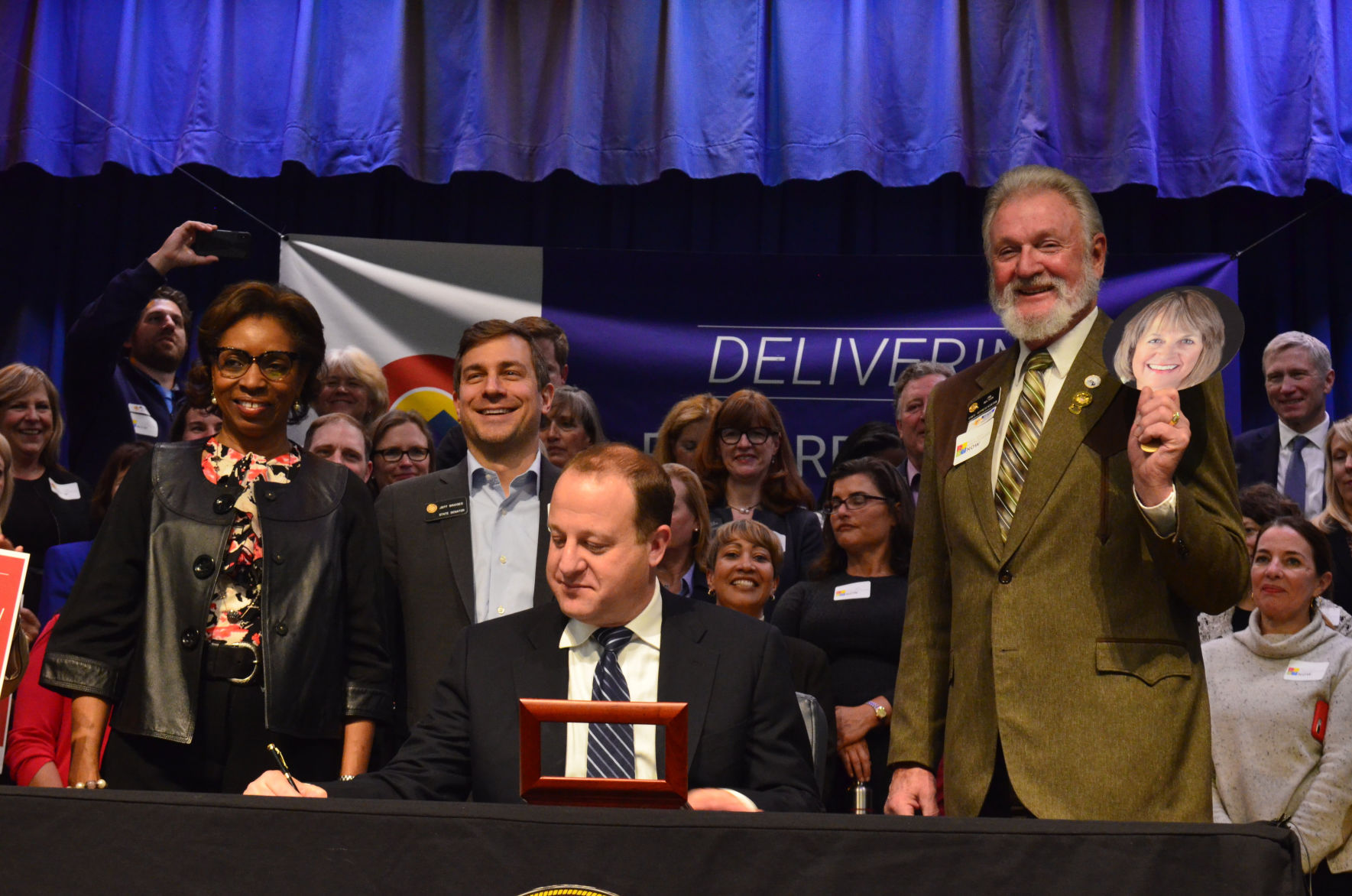 Republican Rep. Jim Wilson of Salida, far right, holds a photo of Rep. Barbara McLachlan, a Democrat from Durango, with home he co-sponsored the legislation to create a free full-day kindergarten program signed into law by Gov. Jared Polis, seated, on May 21, 2019 in Denver. (JoeyBunchjoey.bunch@coloradopolitics.comhttps://secure.gravatar.com/avatar/66505e98f9e3fed10e6a3b9a1fc4ca22?d=mm&r=g)