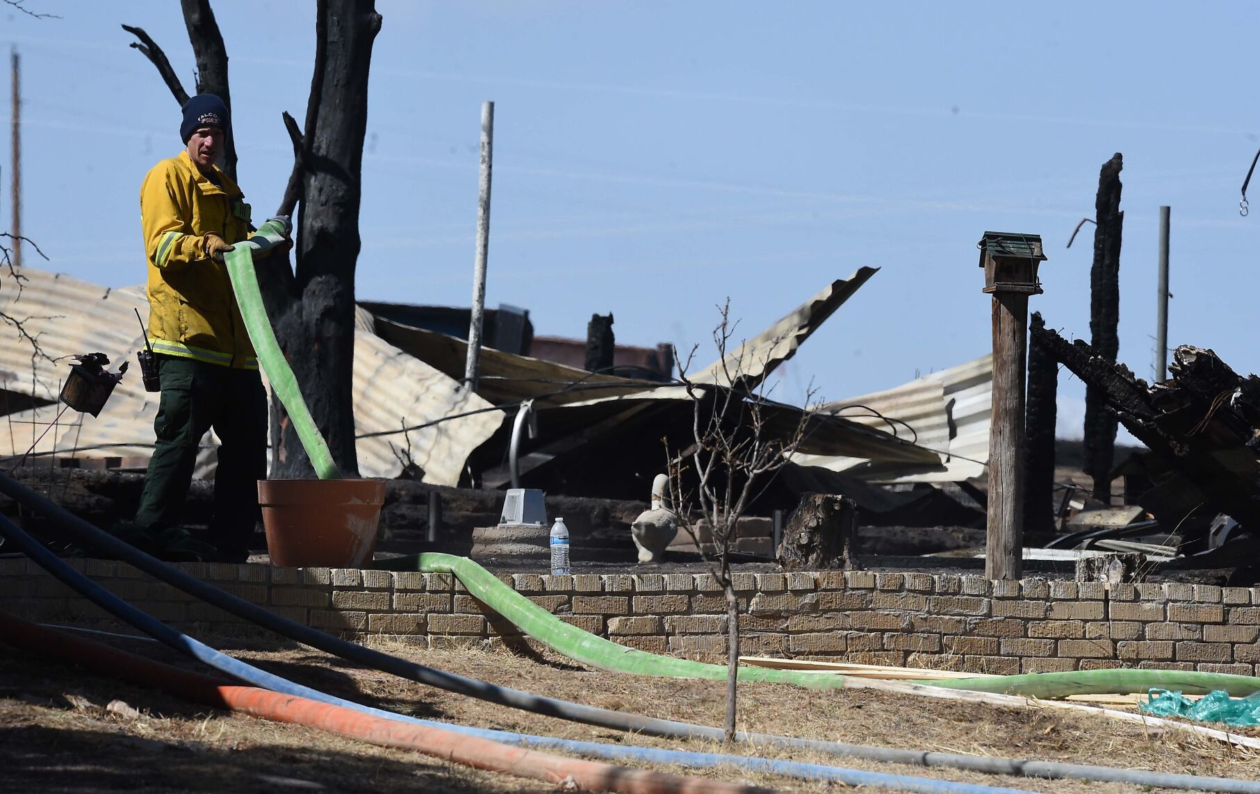 A firefighter rolls up a hose at the home that burned to the ground during a brush fire off of Curtis Rd. on Sunday night. Members of the Falcon Fire Dept. monitored the fire area into the morning on Monday, April 11, 2022. .(Photo by Jerilee Bennett, The Gazette) (Jerilee Bennett)
