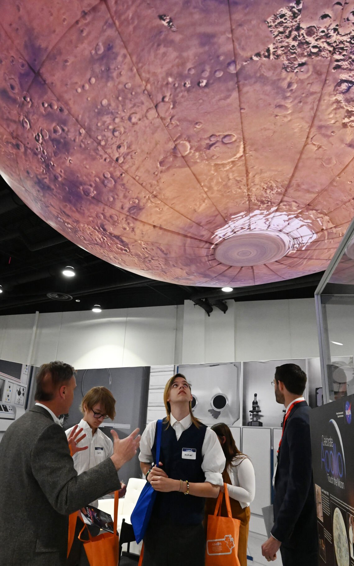 Mitchell High School student Michael Wofford looks up at a large spherical model of Mars on display while listening to his teacher, John Lewis (left). Wofford and other area STEM students were touring the exhibits on the last day of the 37th Space Symposium on Thursday, April 7, 2022. (Photo by Jerilee Bennett, The Gazette) (Jerilee Bennett, The Gazette)