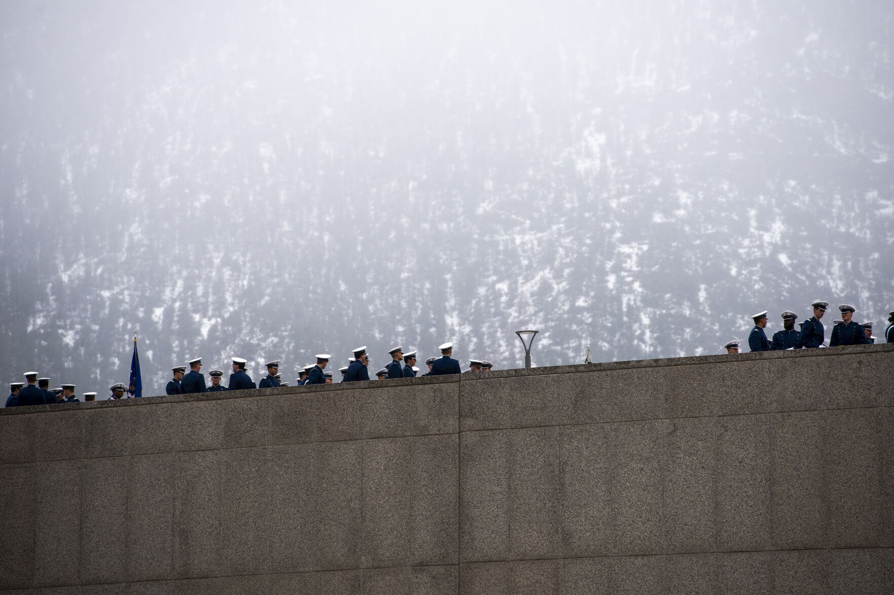 Snow creates a bright backdrop on the mountain as cadets line up before marching onto Stillman Parade Field at the Air Force Academy graduation parade on Tuesday, May 24. (Parker Seibold / The Gazette) (Parker Seibold / The Gazette)