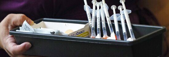 Syringes filled with Pfizer vaccines are brought to vaccinators at a COVID-19 vaccination clinic.