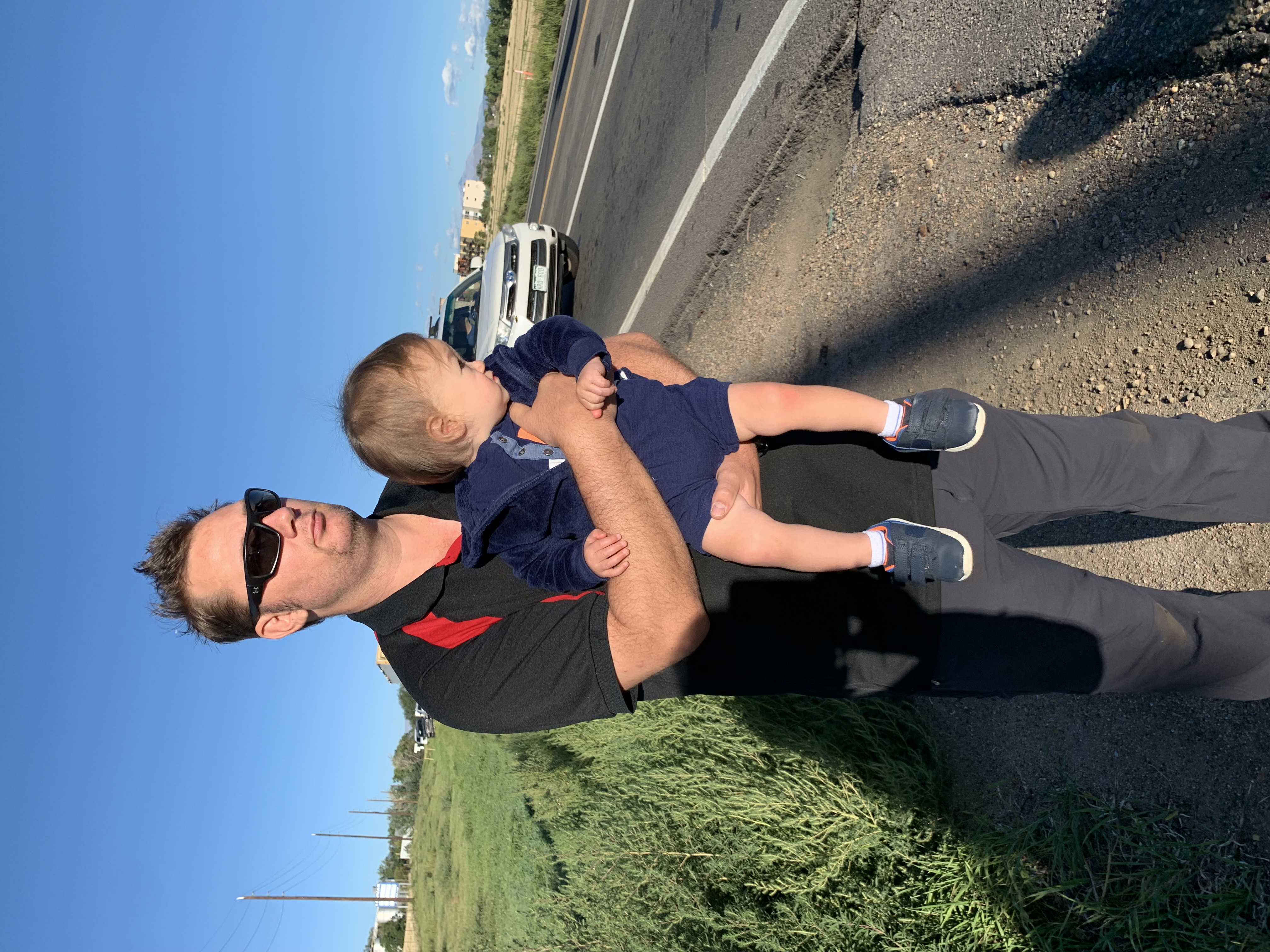 Chris Whiteman, 37, of Superior and his 16-month old son Micah watch the procession of police cars going to the funeral of Arvada Police Ofc. Dillon Vakoff Friday morning off Colorado Highway 7 and 119th Street in Lafayette. Vakoff's memorial service was at Flatirons Community Church. (DENNIS HUSPENI/THE DENVER GAZETTE)