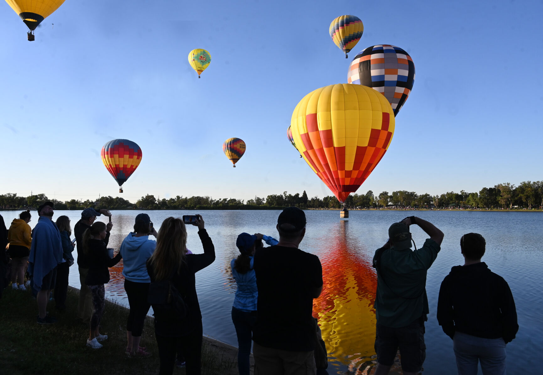 A balloon dips in Prospect Lake while photographers snap away with cameras and phones on the second day of the Labor Day Lift Off on Sunday, Sept. 4, 2022. (Photo by Jerilee Bennett, The Gazette) (Jerilee Bennett)