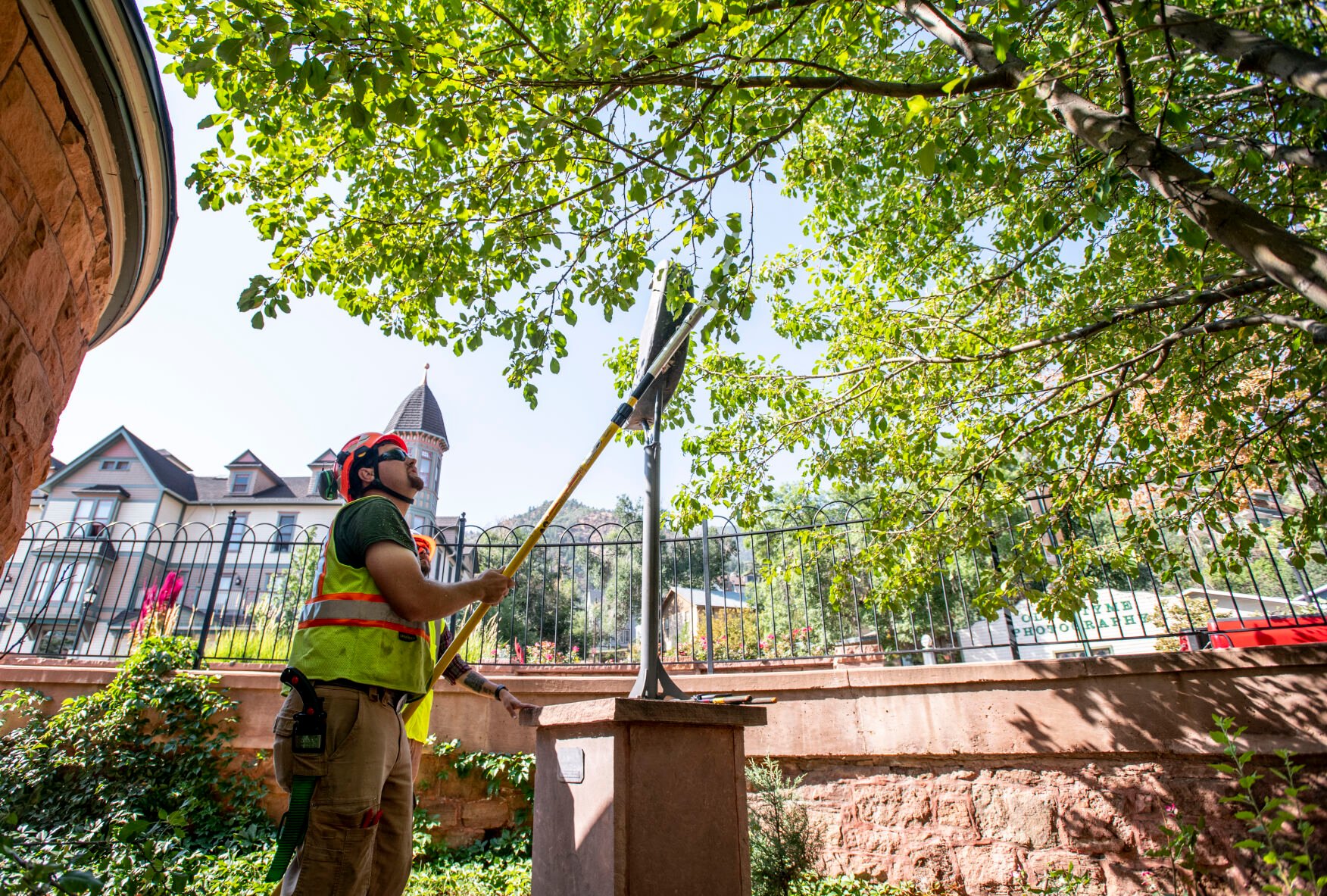 Manitou Springs City Arborist Matthew Weber trims a tree that has grown over a statue next to Shoshone Springs on Manitou Avenue on Friday, Sept. 9, 2022. (The Gazette, Parker Seibold) (Parker Seibold/ The Gazette)