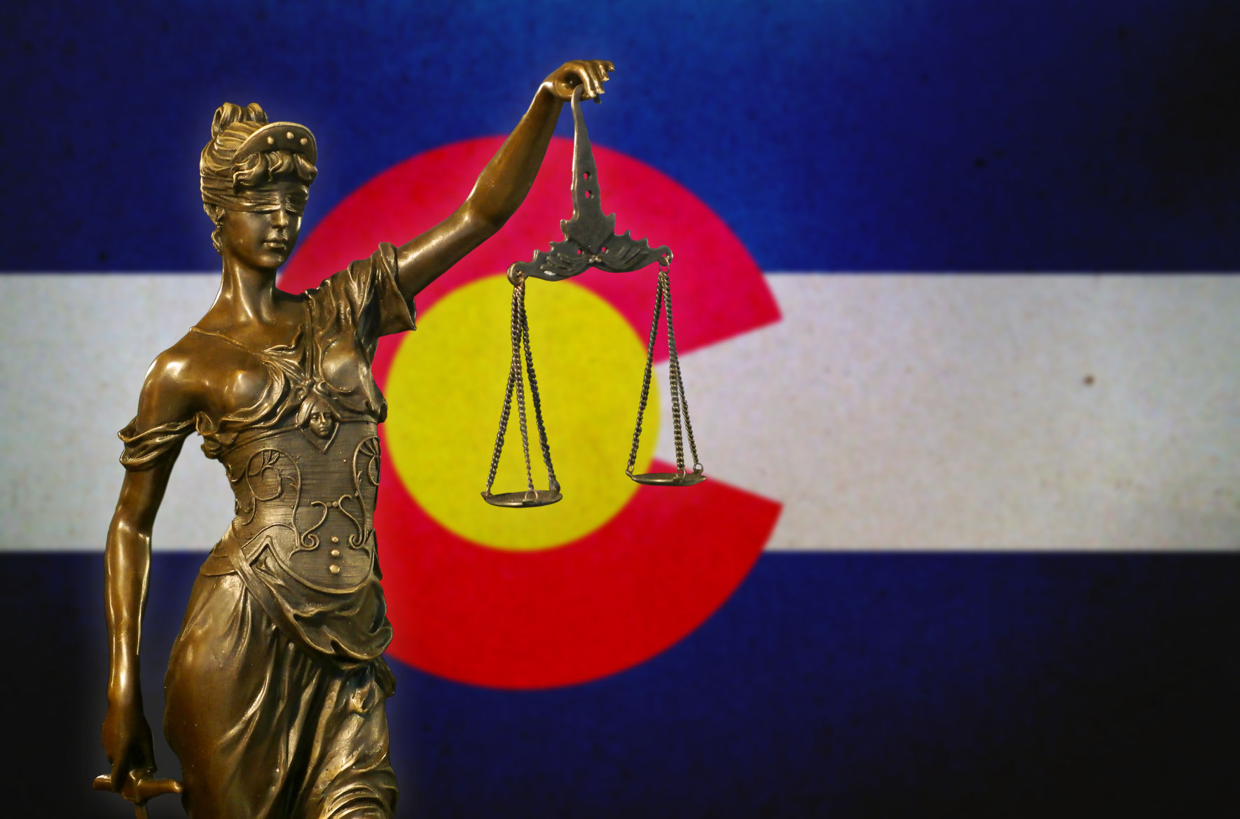 FILE ART: Close-up of a small bronze statuette of Lady Justice before a flag of Colorado. (COURTESY OF GWENGOAT)