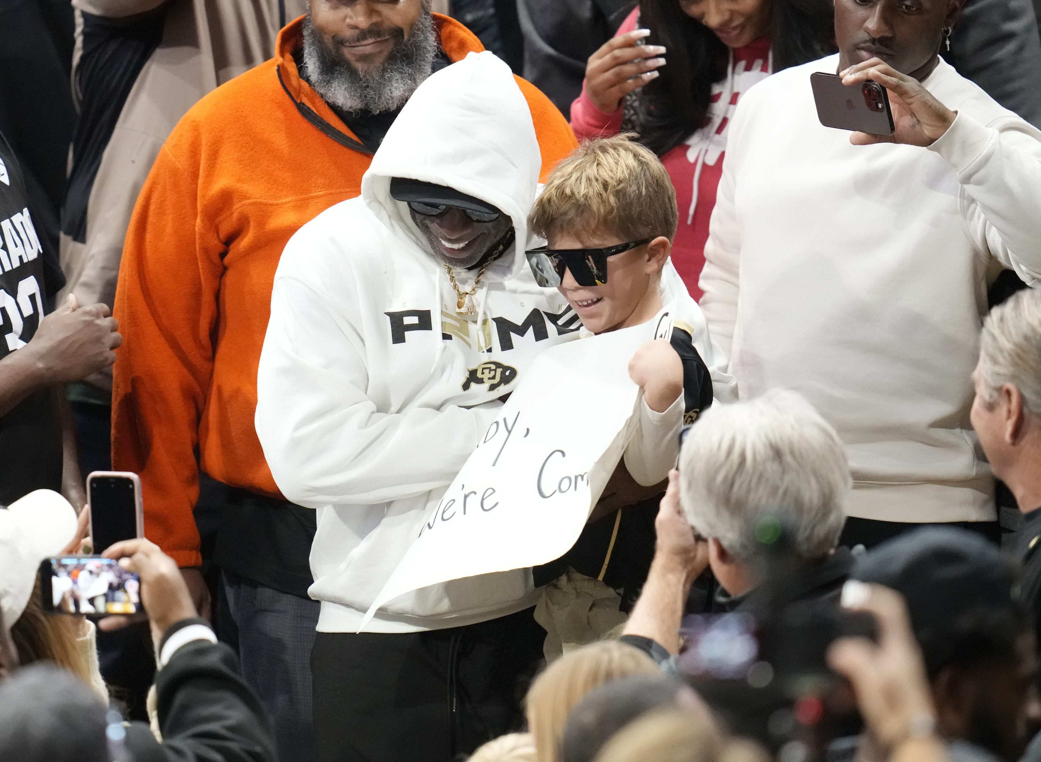Colorado football coach Deion Sanders, left, picks up a young fan holding a sign during the second half of an NCAA college basketball game between Colorado State and Colorado on Thursday, Dec. 8, 2022, in Boulder, Colo. (AP Photo/David Zalubowski) (David Zalubowski)