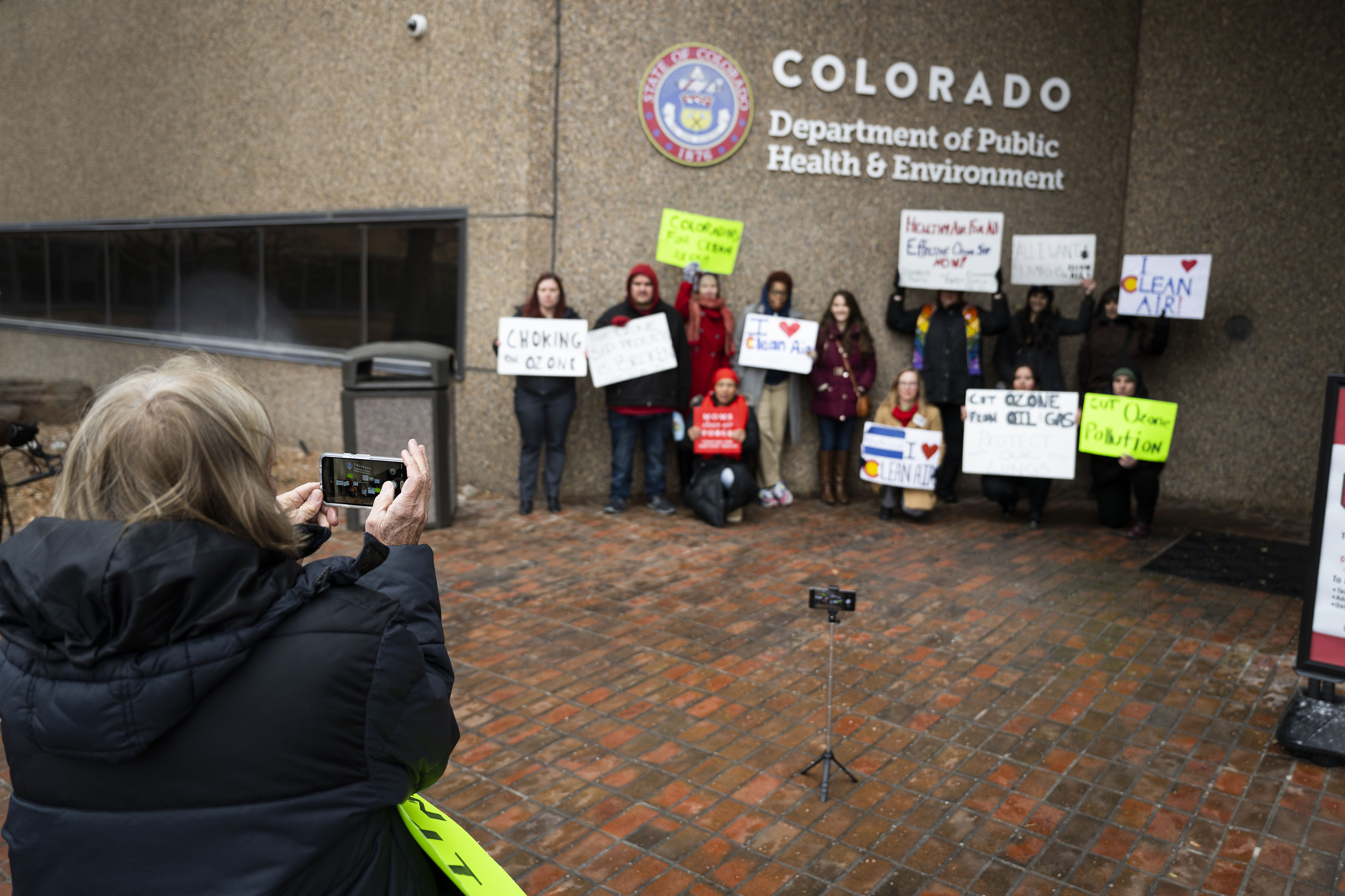 Leslie Glustrom, with Clean Energy Action, takes a group picture of participants in front of the Colorado Department of Public Health and Environment building on Tuesday, Dec. 13, 2022, in Denver, Colo. Participants were there with signs to both take a group photo and give video testimonials on the need to reduce air pollution. (Timothy Hurst/The Denver Gazette) (TimHursttim.hurst@gazette.comhttps://secure.gravatar.com/avatar/aca82bd62b4ee425c598527cd6faa1b1?d=mm&r=g)