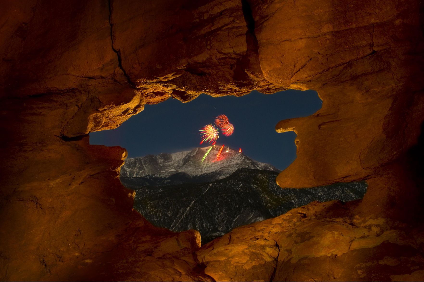 The AdAmAn Club shoots fireworks off the summit of Pikes Peak to welcome the new year, as seen through the Siamese Twins rock formation in Garden of the Gods in Colorado Springs. This photograph was a 45-second time exposure taking advantage of a full moon lighting Pikes Peak. (the denver gazette file)