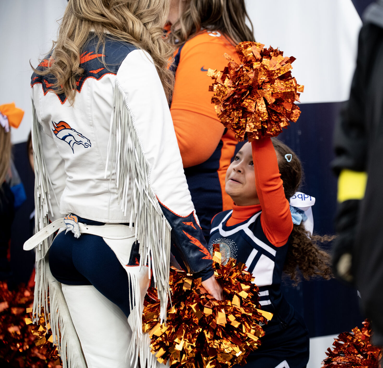 A junior Denver Broncos cheerleader looks up at a Broncos cheerleader before performing at halftime Sunday, Jan. 8, 2023 at Empower Field at Mile High in Denver. (Parker Seibold, The Gazette) (Parker Seibold)
