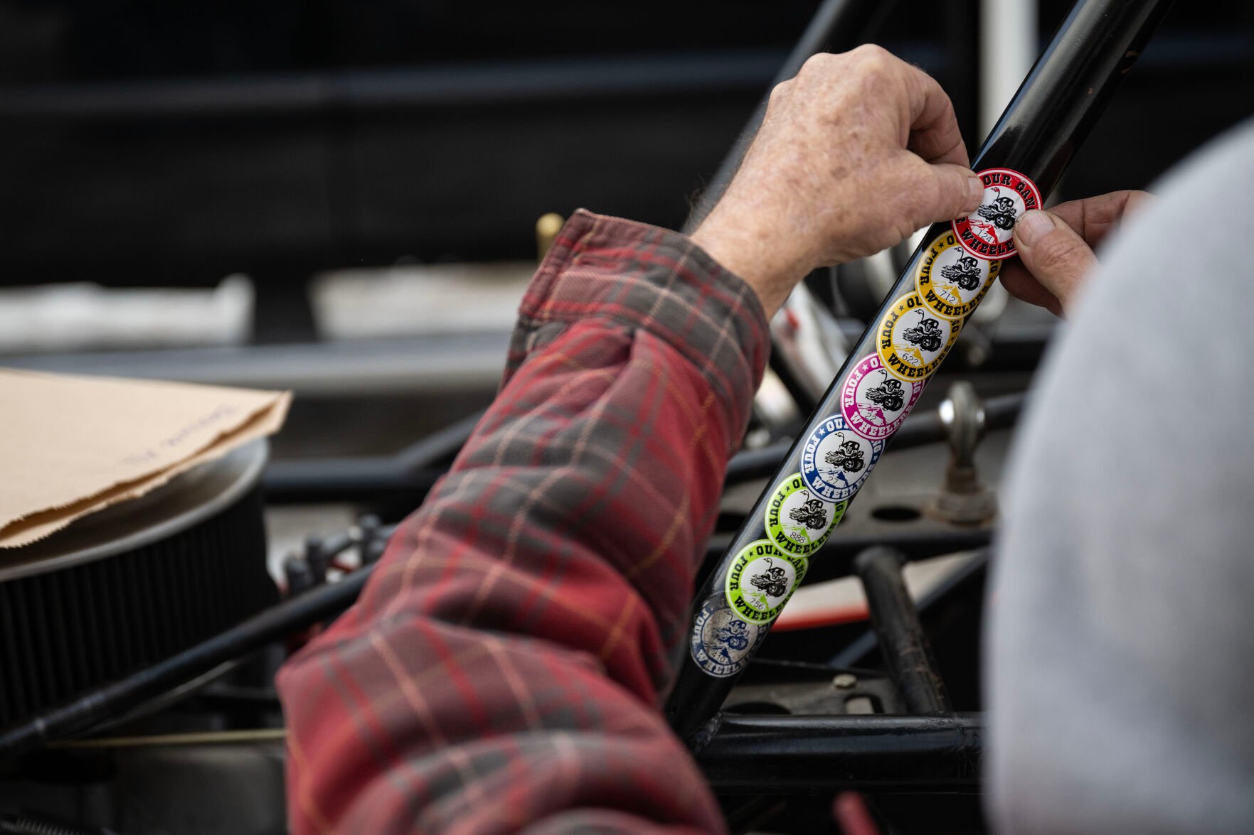 Seasoned ice driver Lee Bashline sticks this year’s new sticker to the roll cage of his highly modified single-seater Willys after passing inspection. (Timothy Hurst, The Gazette)
