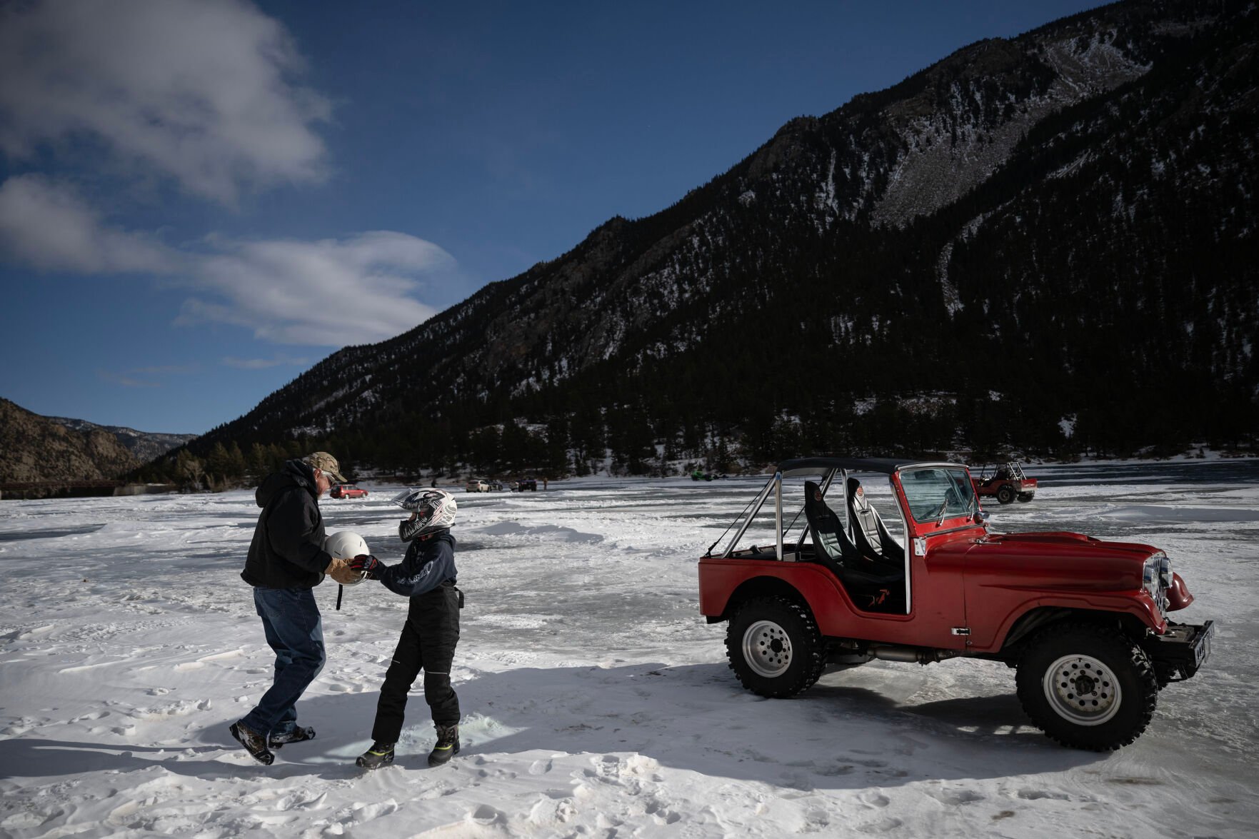 Cooper Altman, 12, hands his grandfather Dave Ling’s helmet to him before taking some practice laps in Ling’s 1976 fiberglass-bodied Jeep during the first day of the Our Gang 4 Wheelers ice racing club’s 2023 racing season on Jan. 7 in Georgetown. (Timothy Hurst, The Gazette)