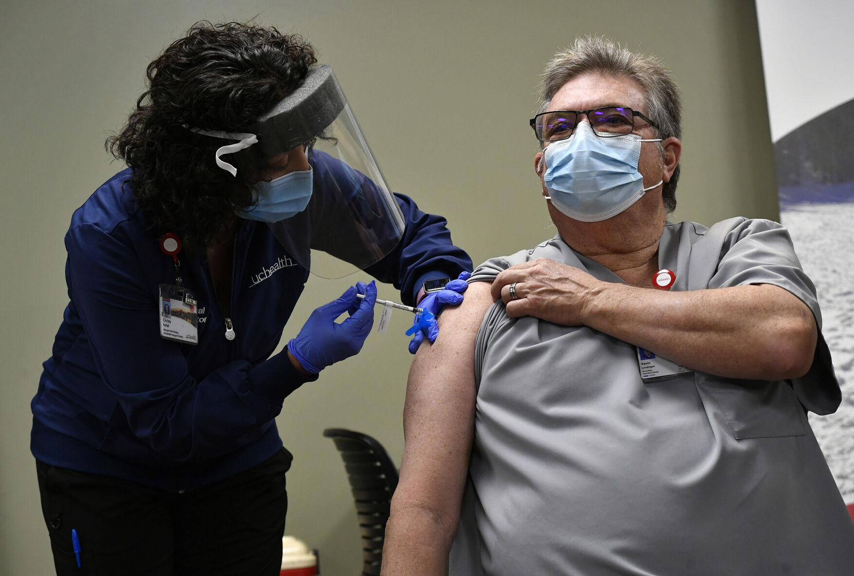 FORT COLLINS, COLORADO - NOVEMBER 14: Christy Ruffell, manager of clinic nursing standards at UCHealth Medical Center, left, administers the very first Covid-19 vaccine to Kevin Londrigan, a respiratory therapist at UCHealth Medical Center, right, at UCHealth Poudre Valley Hospital on December 14, 2020 in Fort Collins, Colorado. The first Covid-19 vaccines were administered in Colorado to frontline health care workers in Fort Collins and Colorado Springs today. Governor Jared Polis joined these nurses, doctors, respiratory therapists and other frontline workers in the cafeteria of hospital as one by one they got the vaccine. A total of twenty vaccines were administered to a variety of doctors, nurses, respiratory therapists and others from Northern Colorado medical facilities. (Photo by Helen H. Richardson/The Denver Post, Pool) (Helen H. Richardson)
