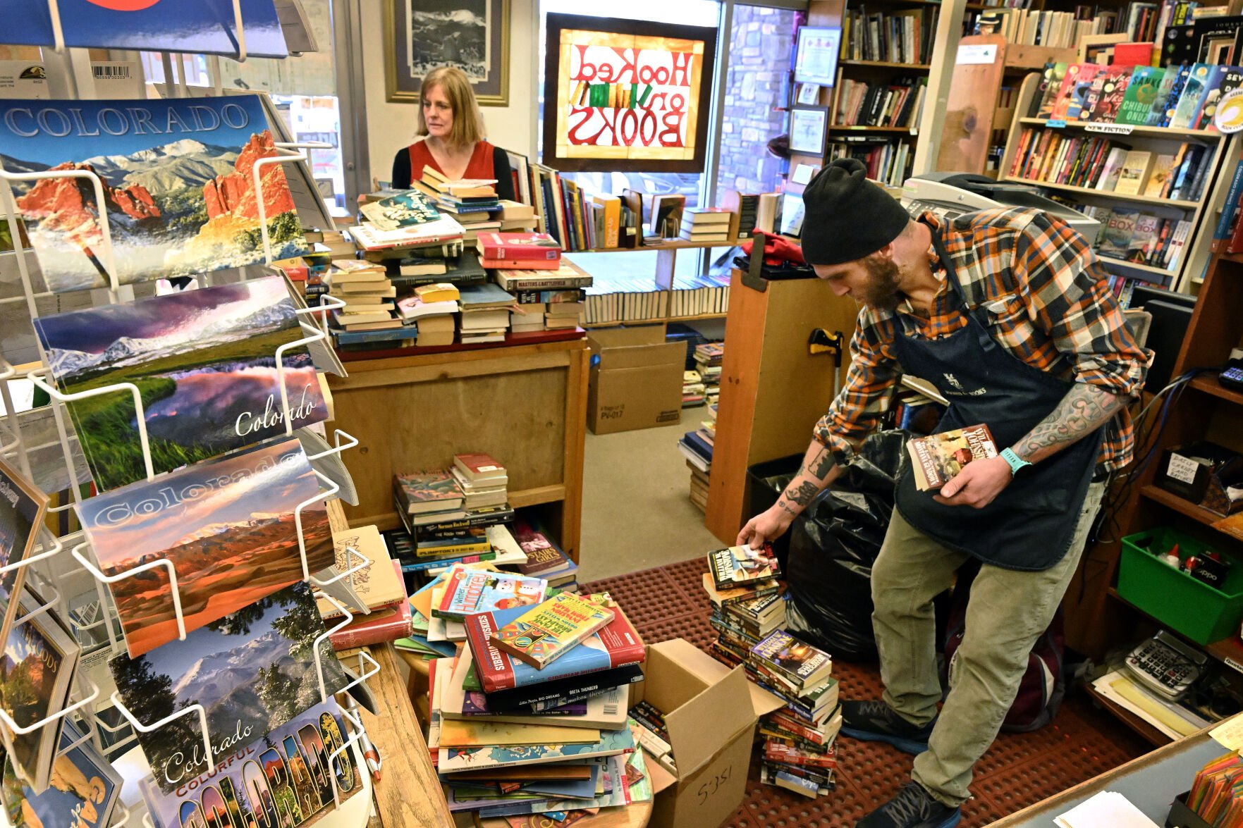 New Hooked on Books shop owner Joseph Shearer gets help from former owner Mary Ciletti, while unpacking a shipment of books on Monday, April 10, 2023. Mary started the Maizland store over 40 years ago and is helping show Joseph and his wife, Mikayla Shearer, the ropes during the transition in ownership. Mary and her husband, Jim Ciletti, will still own and operate the Hooked on Books store downtown. (Photo by Jerilee Bennett, The Gazette)