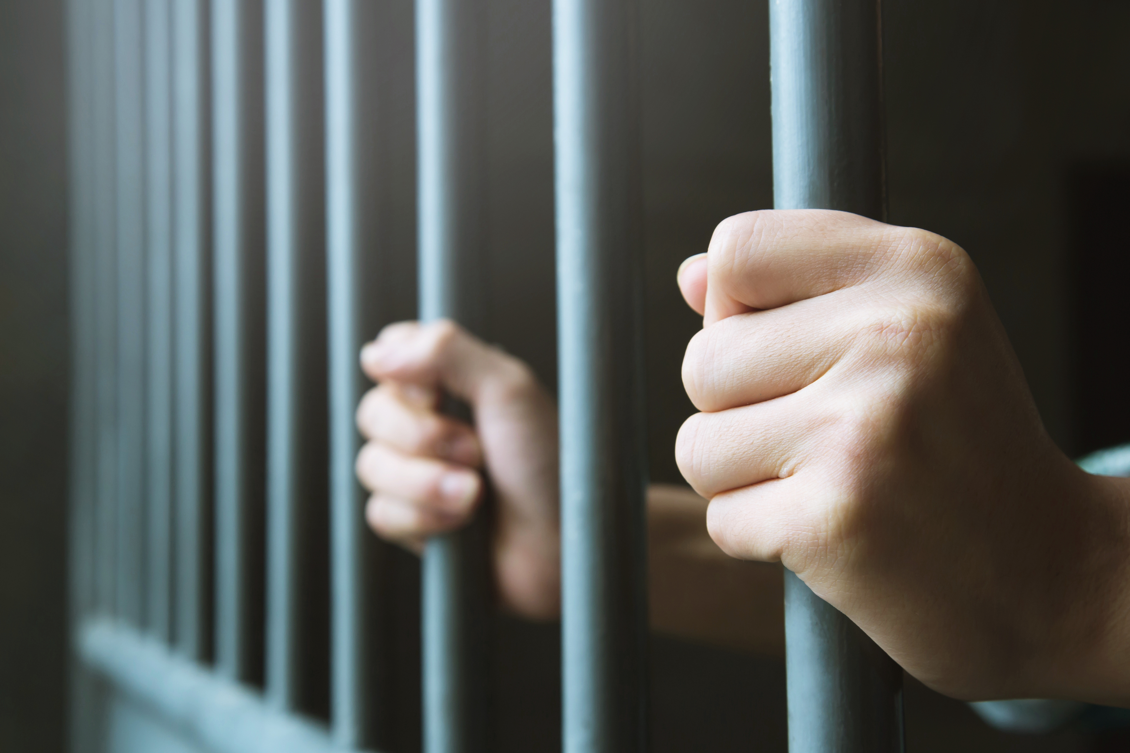 Man in prison hands of behind hold Steel cage jail bars. offender criminal locked in jail. (Rattankun Thongbun / iStock)